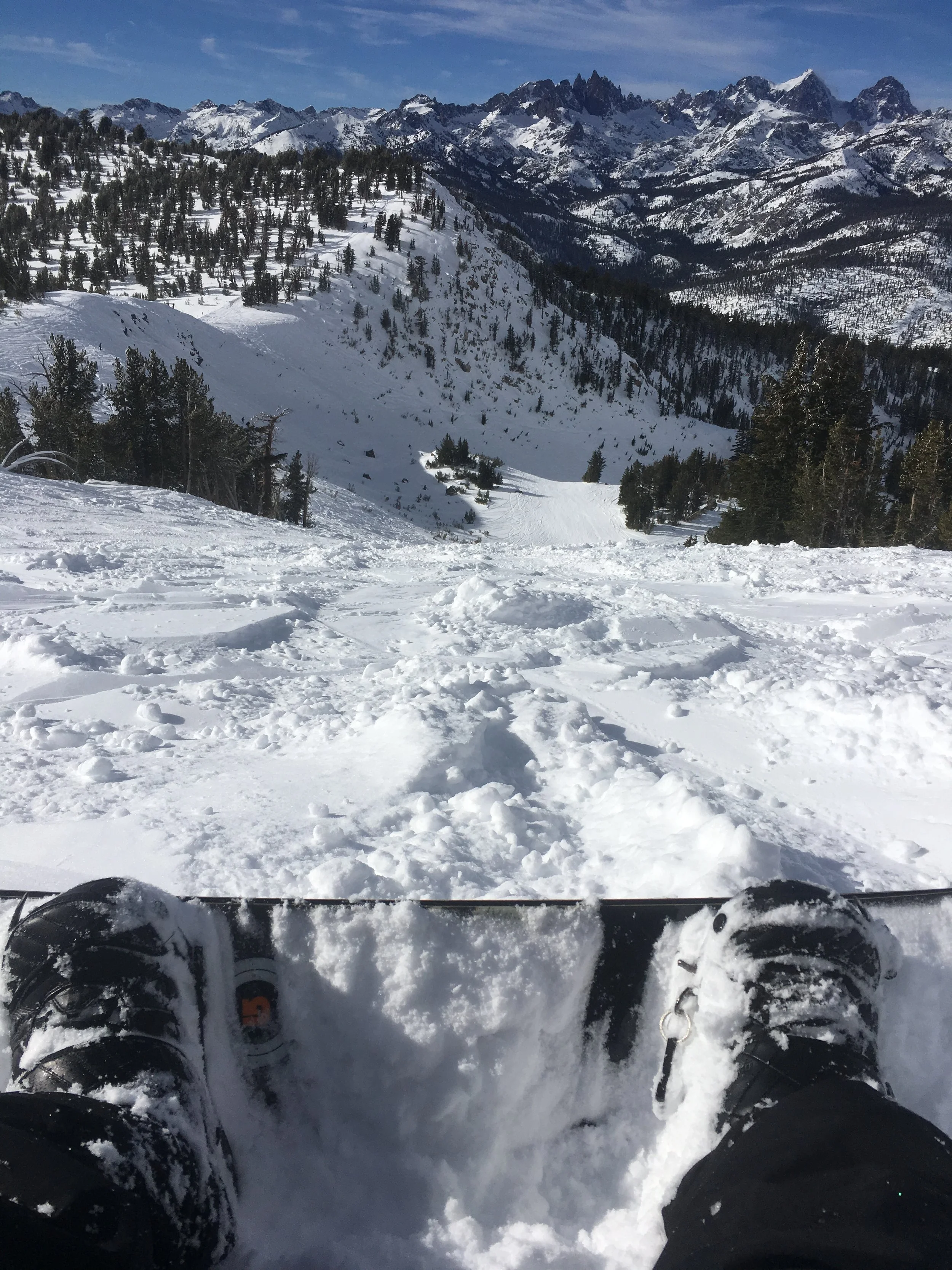 View from a snow-covered mountain during a ski or snowboarding trip, with ski boots visible in the foreground and a mountain landscape in the background.
