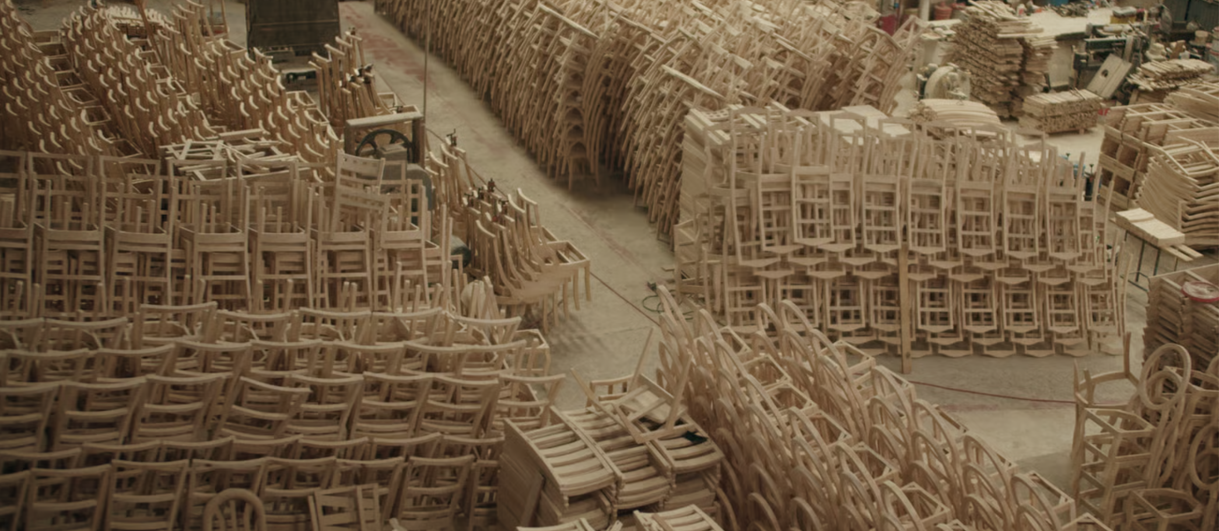 A large workshop with organized stacks of wooden chairs in various stages of assembly.
