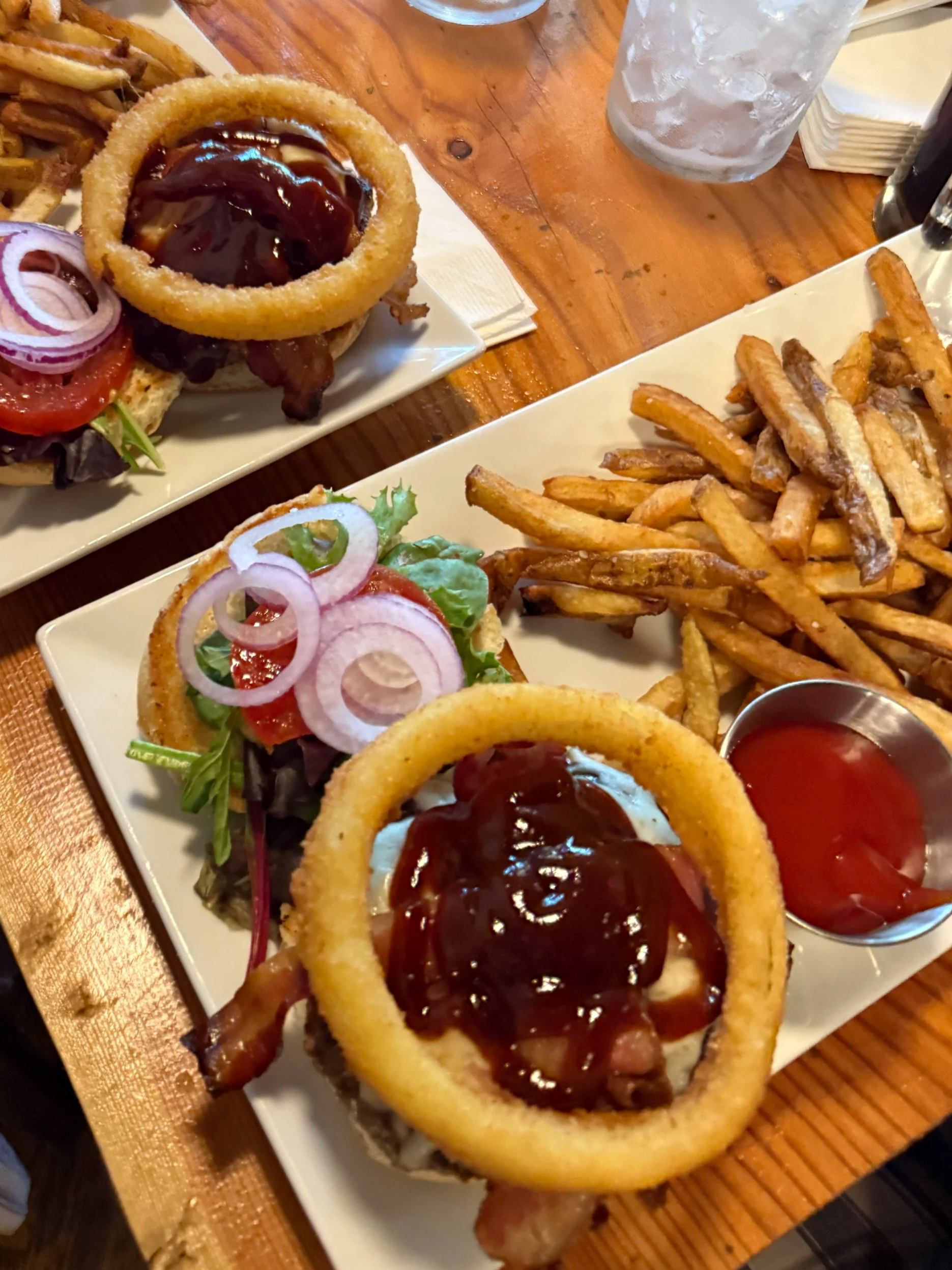 Two plates of food with burgers, French fries, and a drink on a wooden table.