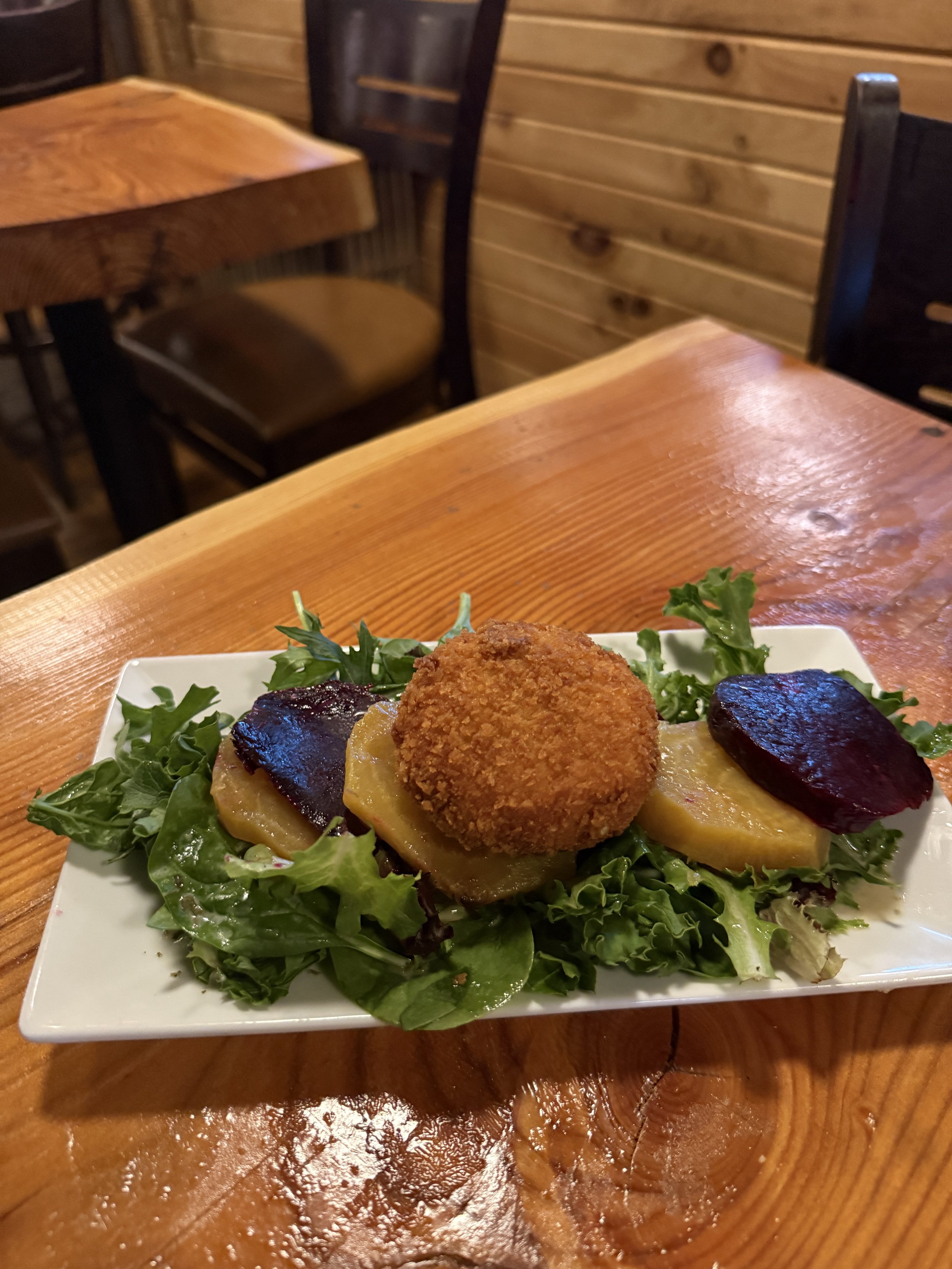 A plate of fried croquettes on a bed of leafy greens with slices of roasted potatoes and beet slices.