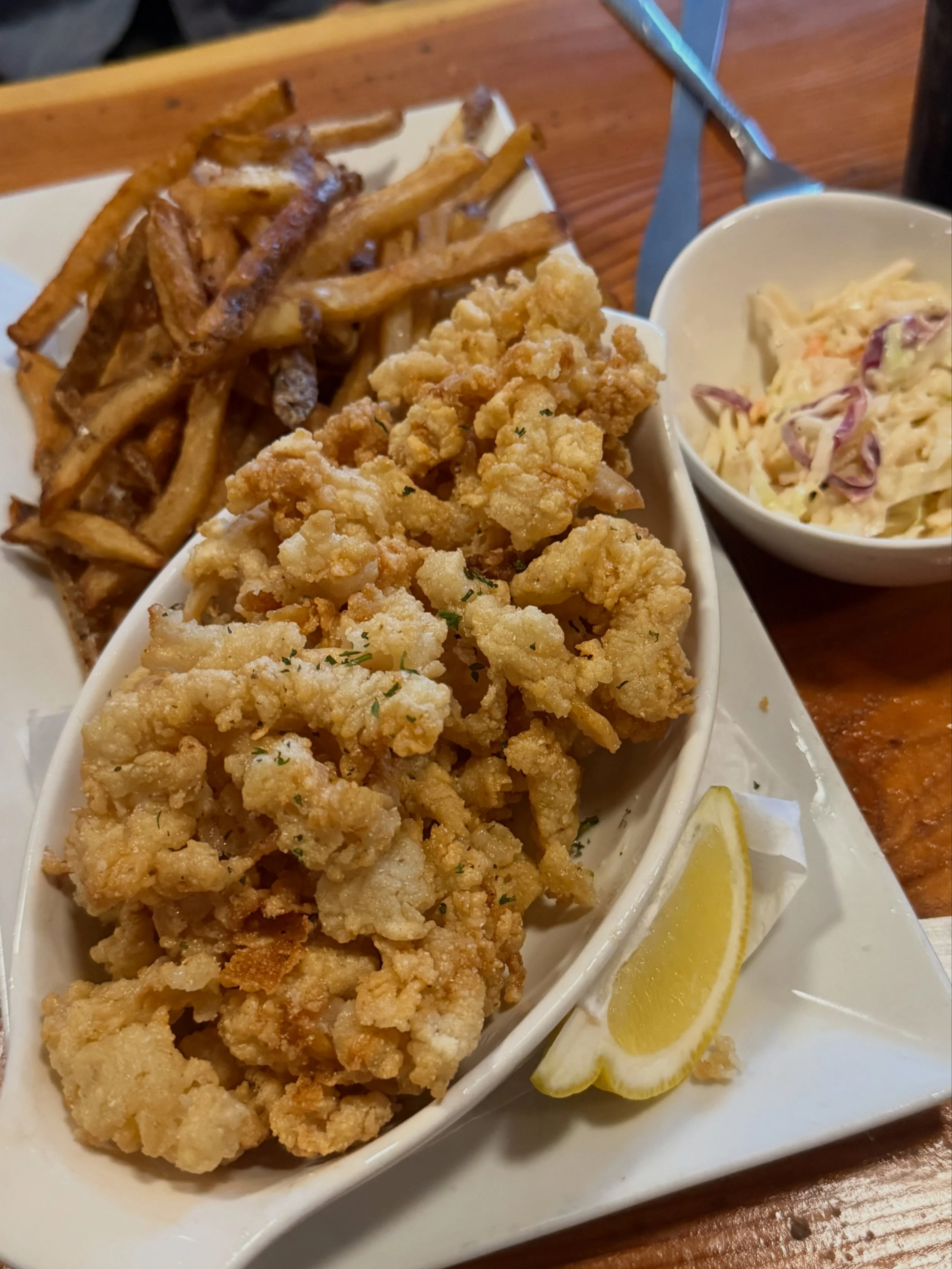 Fried chicken tenders, French fries, side coleslaw, and lemon wedges on a white plate.
