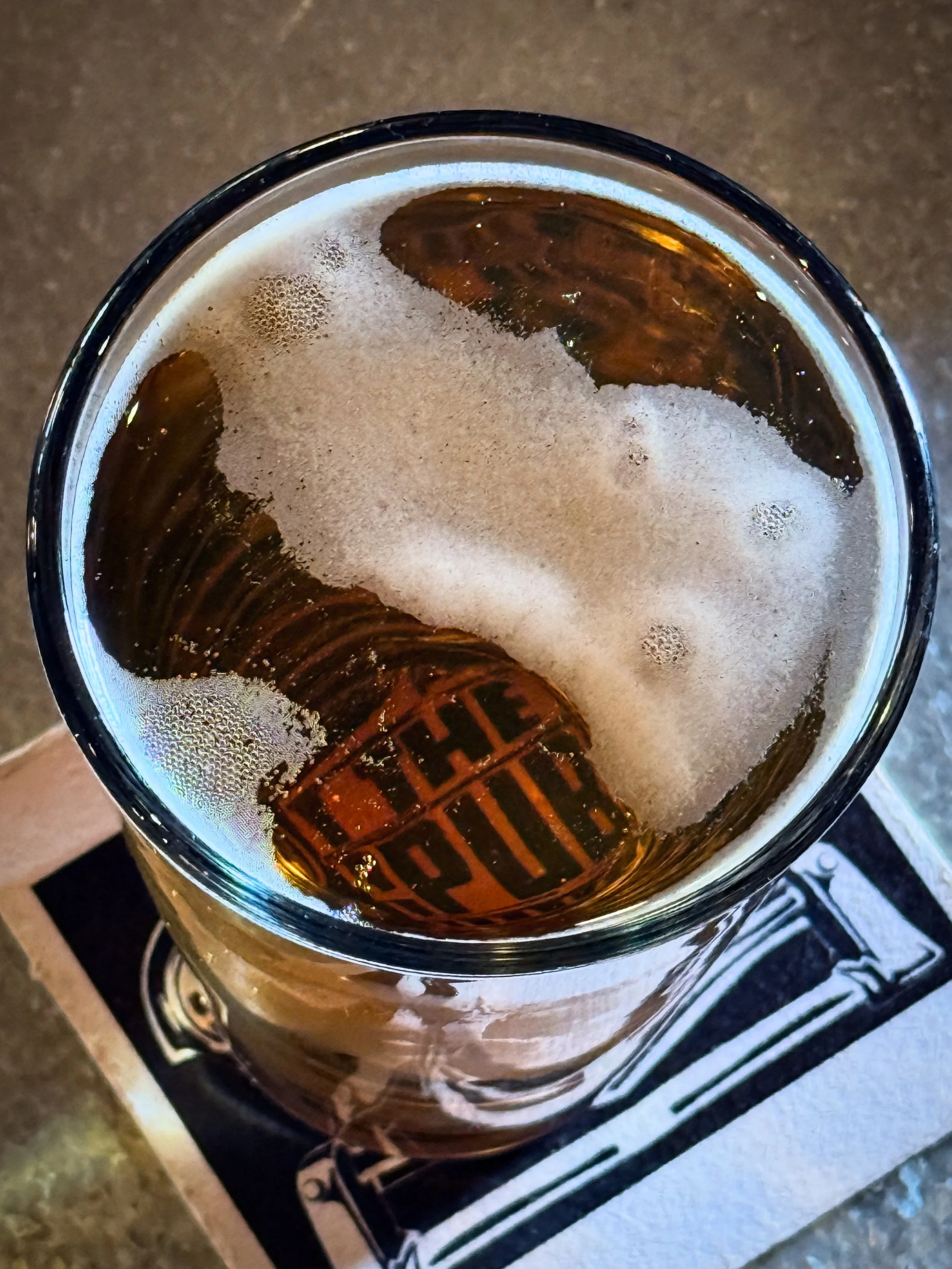 Top view of a glass of dark soda with ice cubes cooling inside, on a stove.