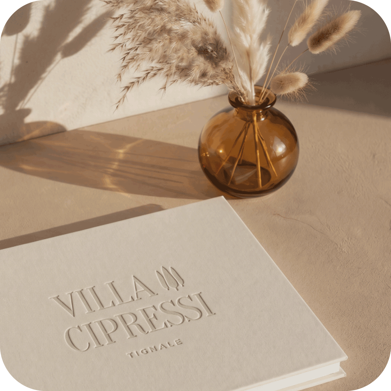 Gästemappe mit geprägtem Logo der Villa Cipressi neben einer Vase mit Trockengräsern