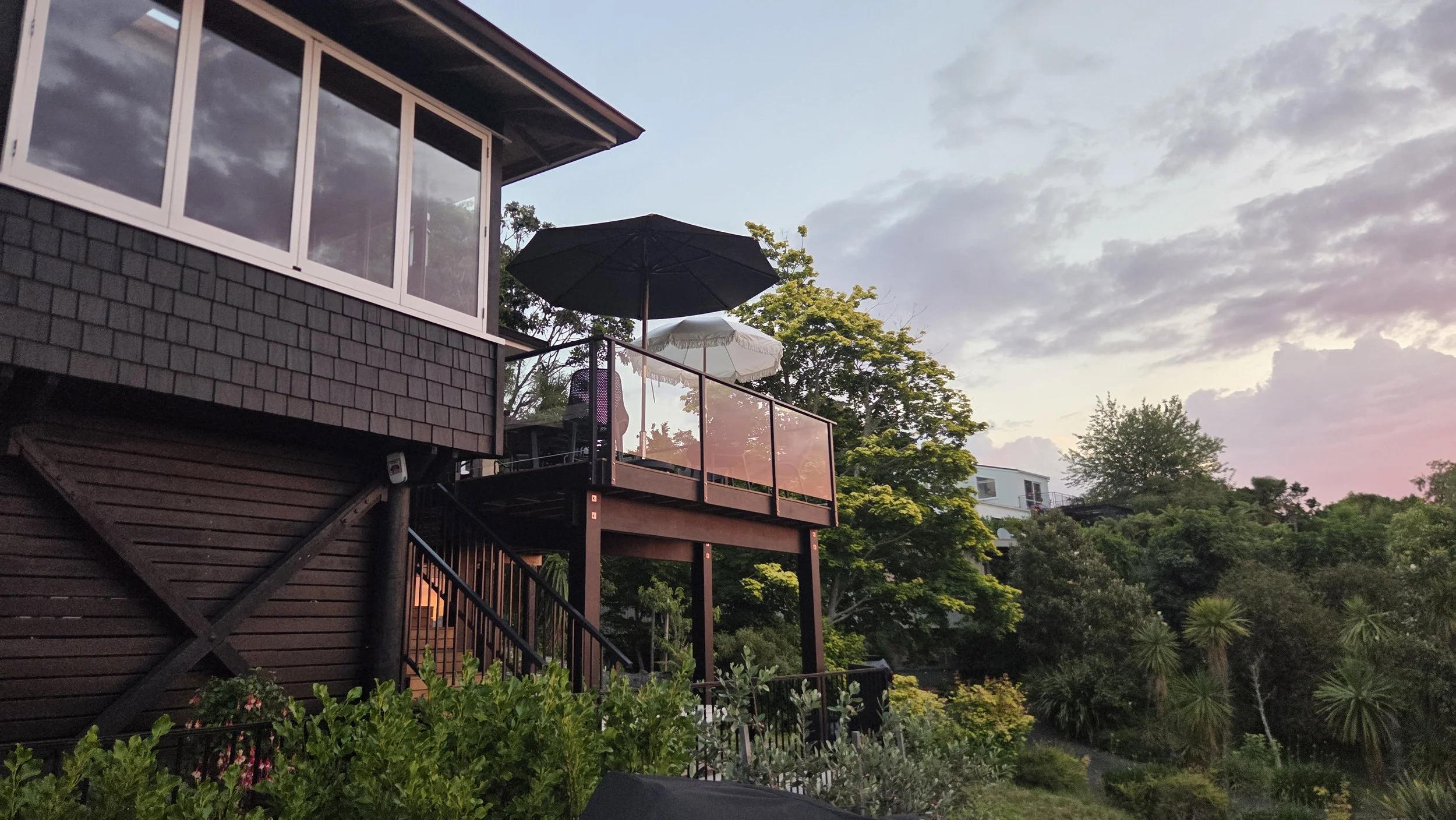 A balcony with an open umbrella and surrounding trees during sunset.