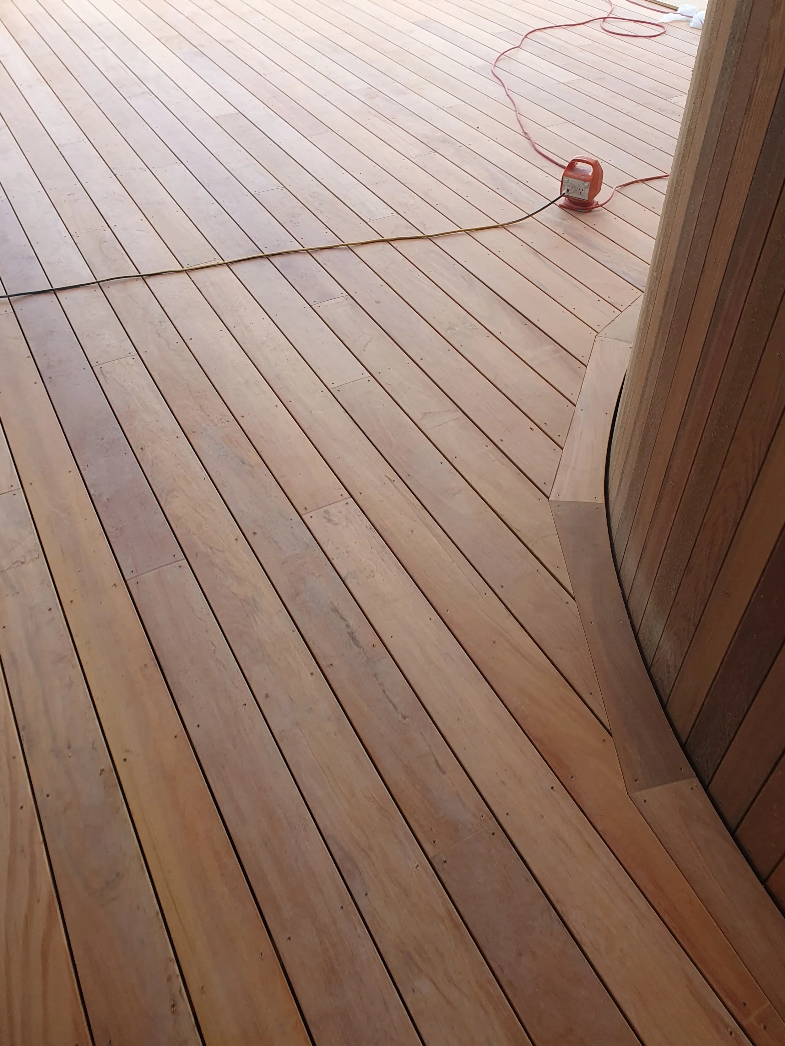 A wooden deck floor with a power cord and an orange extension cord reel.