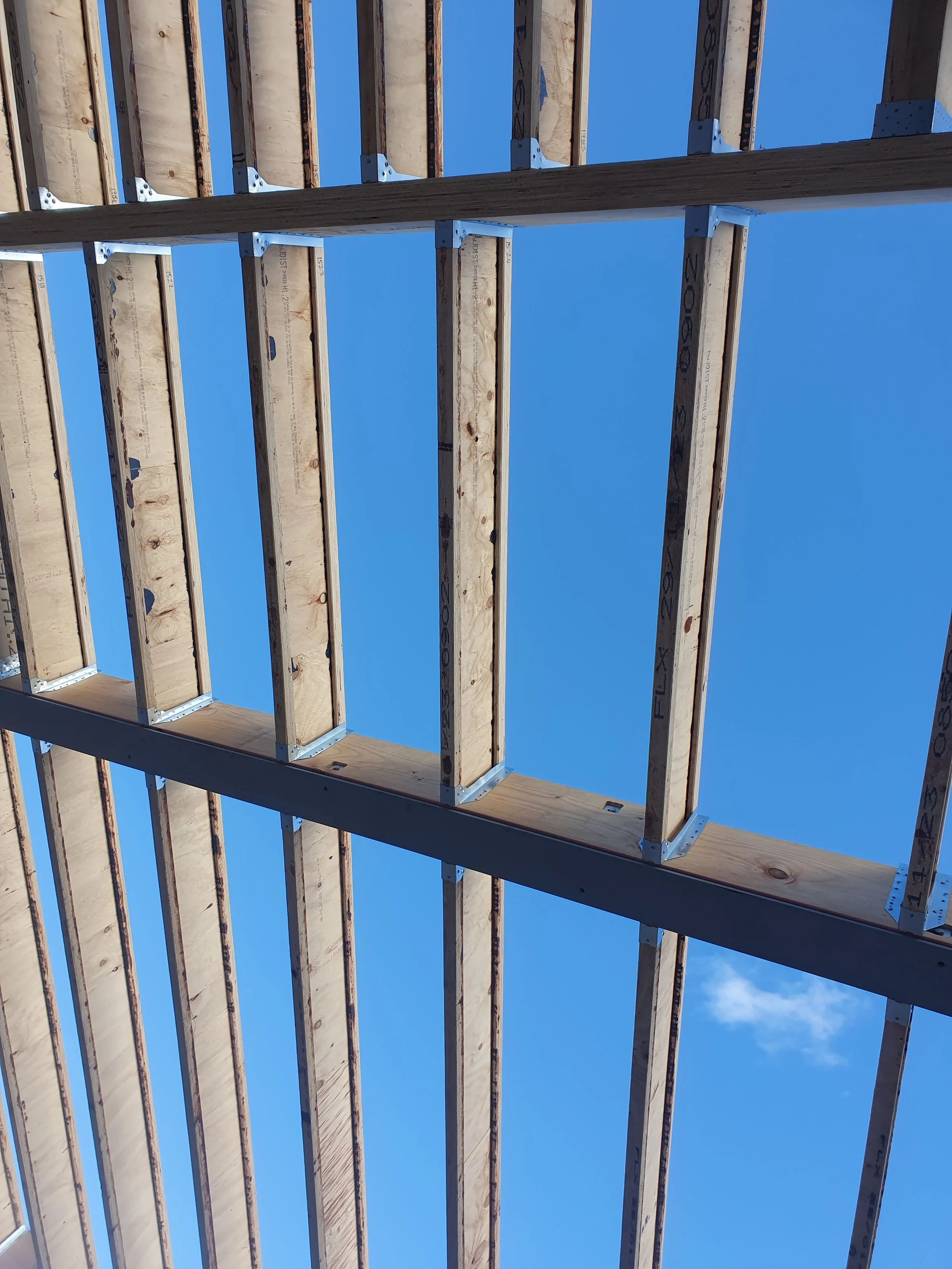 Wooden building framework under construction with exposed beams and supports, blue sky overhead.