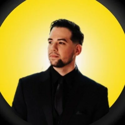 Portrait of a man in a black suit against a yellow background.