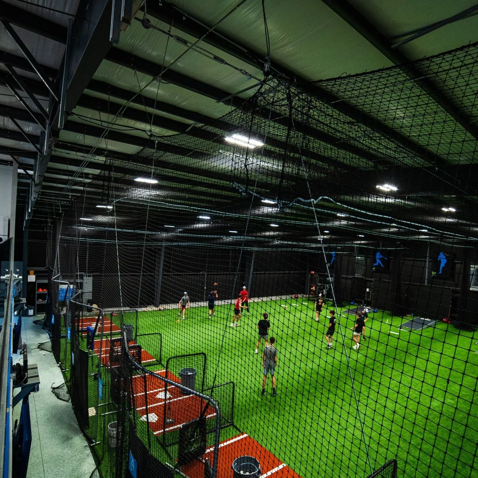 Velocity Sports, indoor sports training facility with a batting cage and a turf field where multiple players are practicing baseball or softball drills.