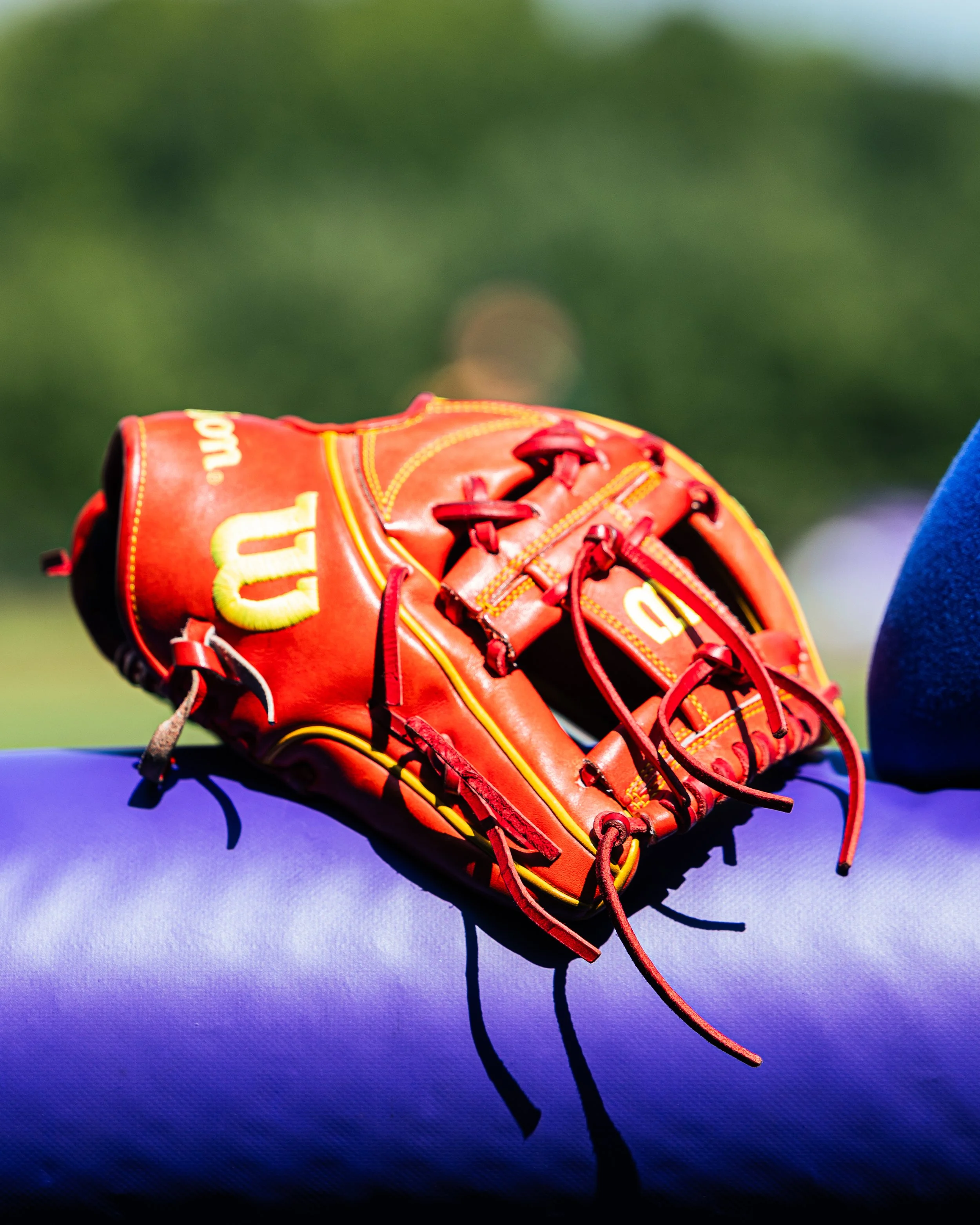 Close-up of a red and yellow baseball glove placed on a purple surface with a blurred green background.