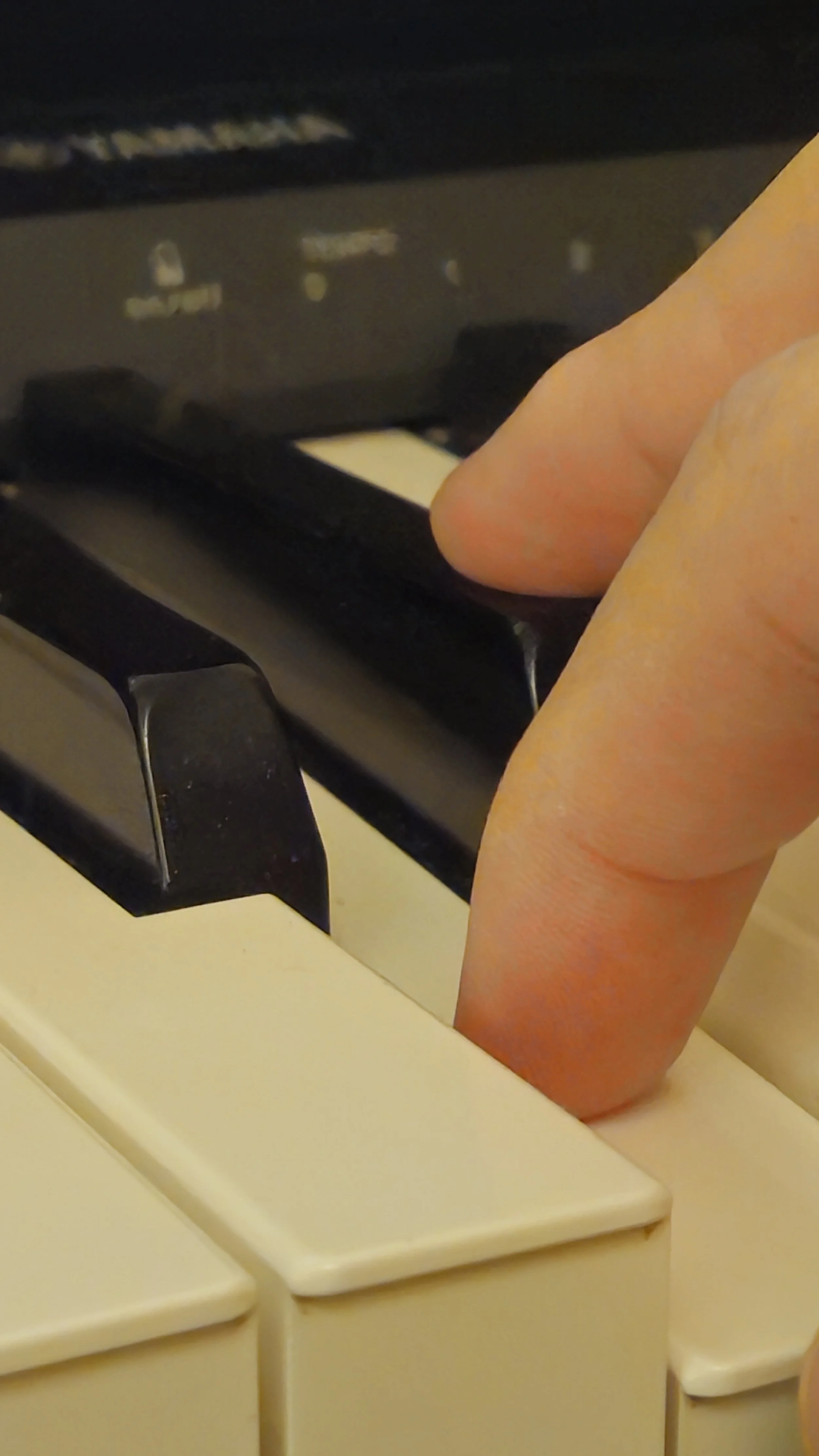 Close-up of a person's thumb pressing a key on a piano keyboard