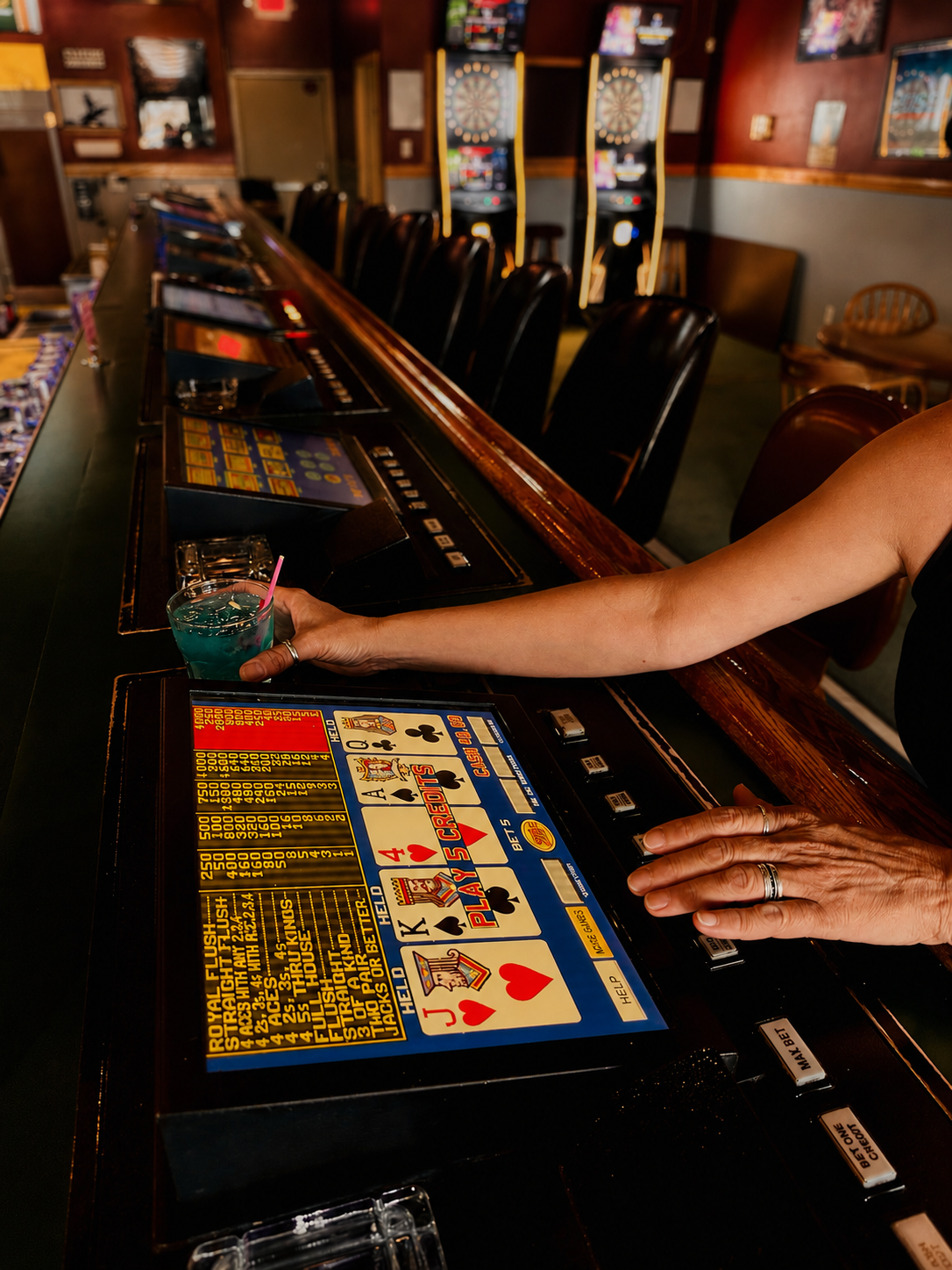 Casino with electronic gaming machines and a person placing a bet at a slot machine, holding a cocktail