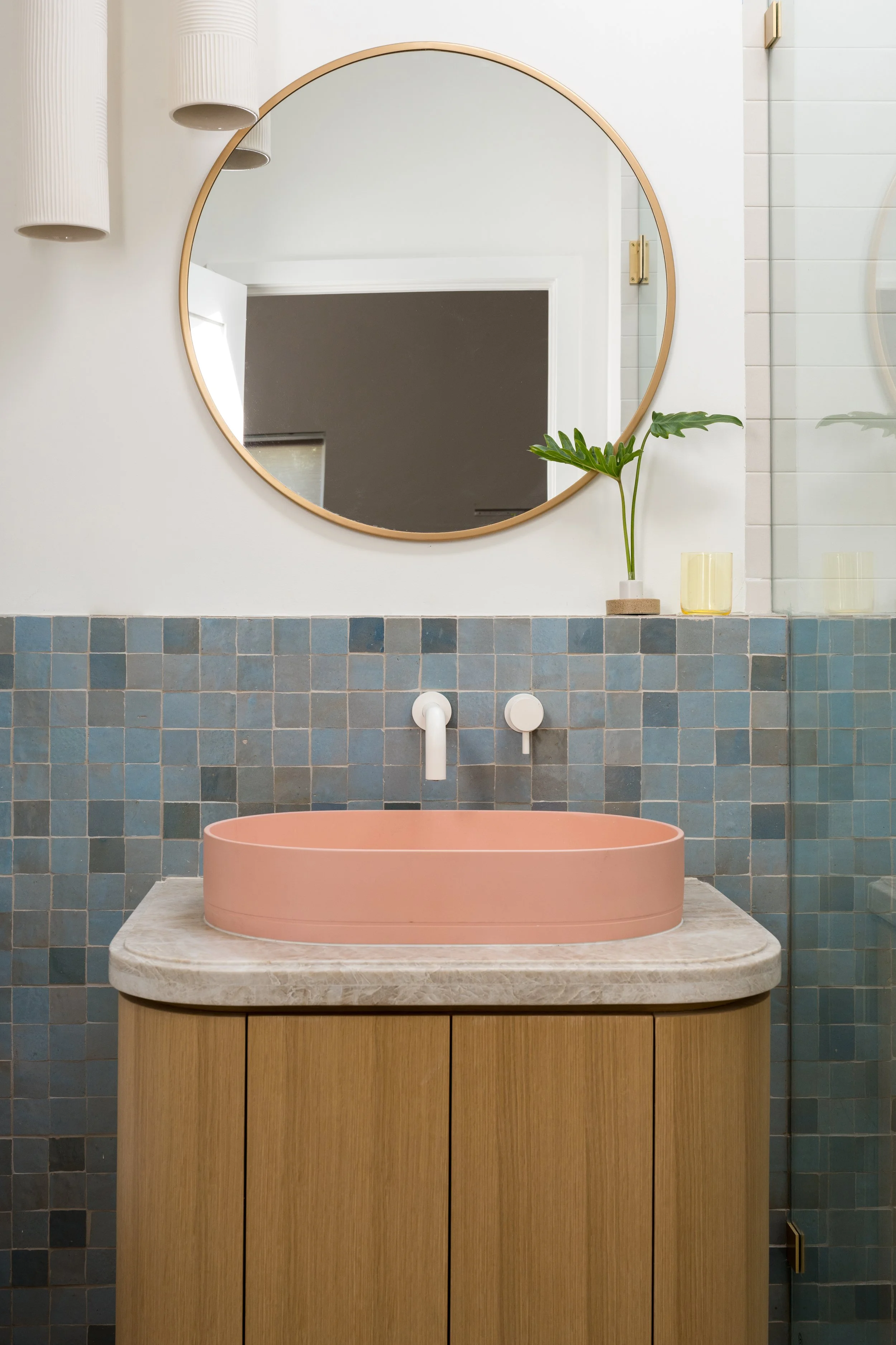 Bathroom with blue, pink, and cream tile walls, wood vanity, and pink sink.
