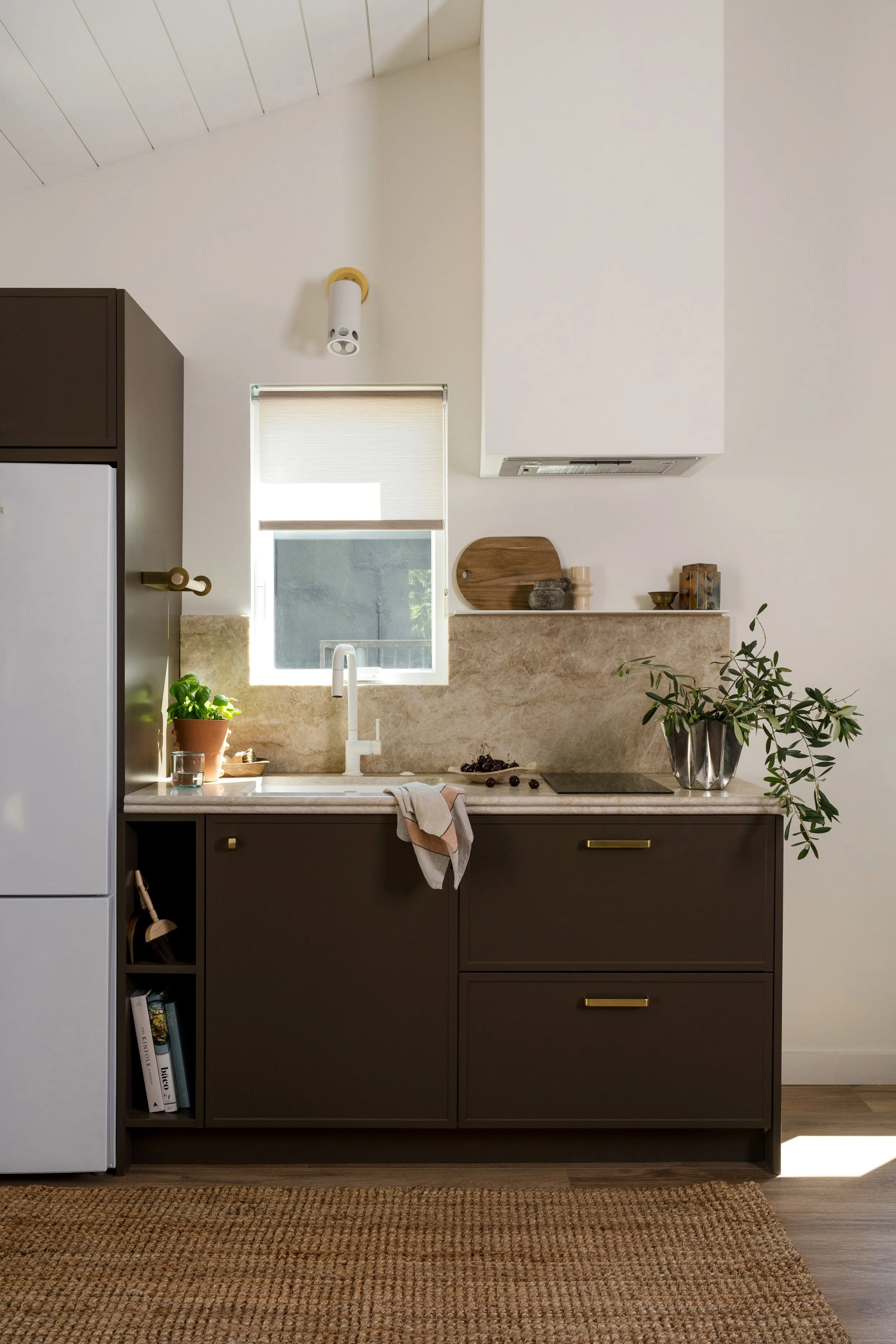 Brown kitchen cabinets paired with a white faucet, natural stone countertops, and full-height stone backsplash.