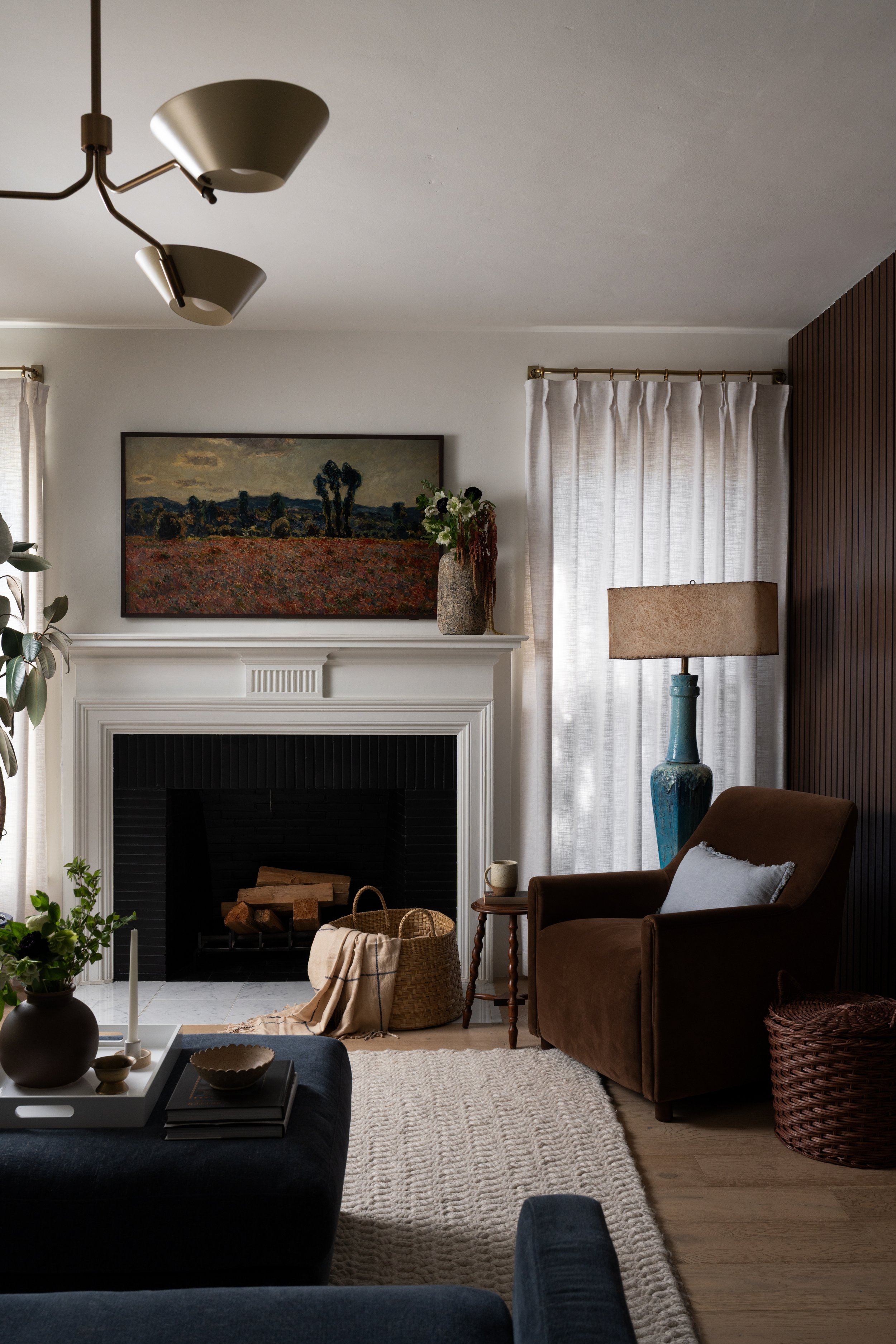 Layered living room with deep blue seating, natural wood accents, neutral curtains, and a fireplace.