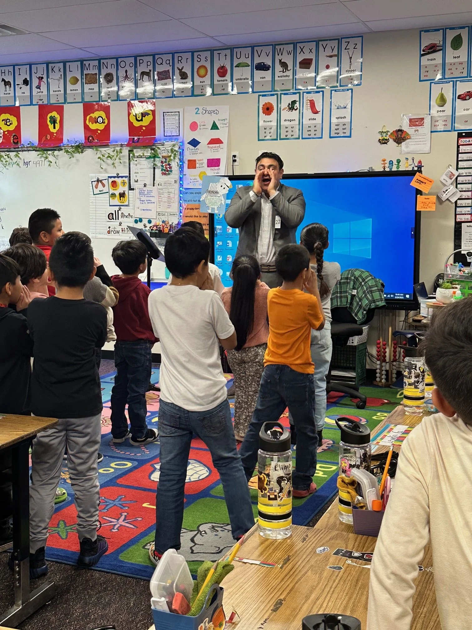 Photograph of a male teacher standing in front of a mixed gender group of students with their backs to the camera. The man has his hands cupped to amplify the sound from his mouth