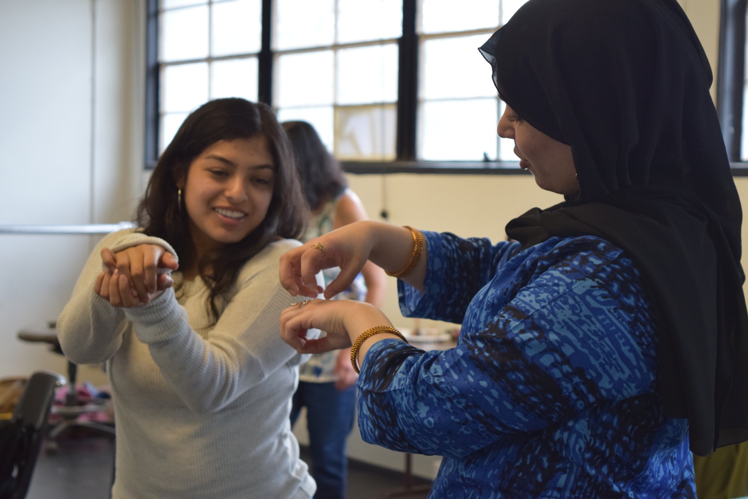 Photograph of teacher wearing hijab and a high school student doing hand movements together