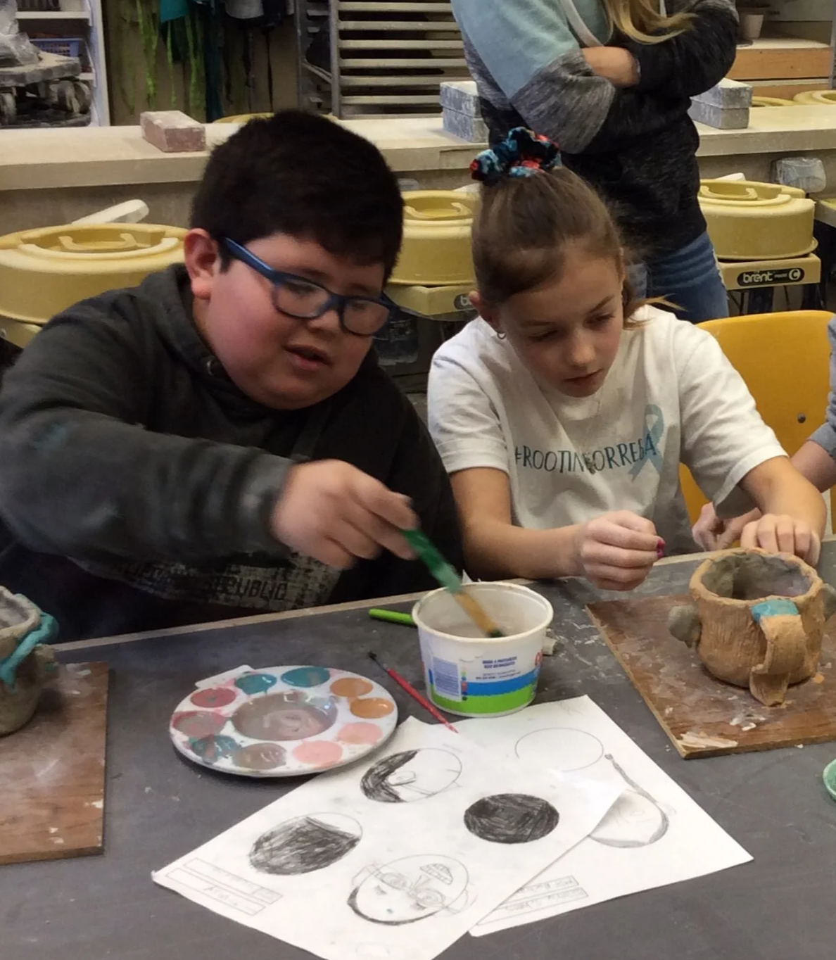 Photograph of elementary age boy and girl painting clay artwork in a studio setting