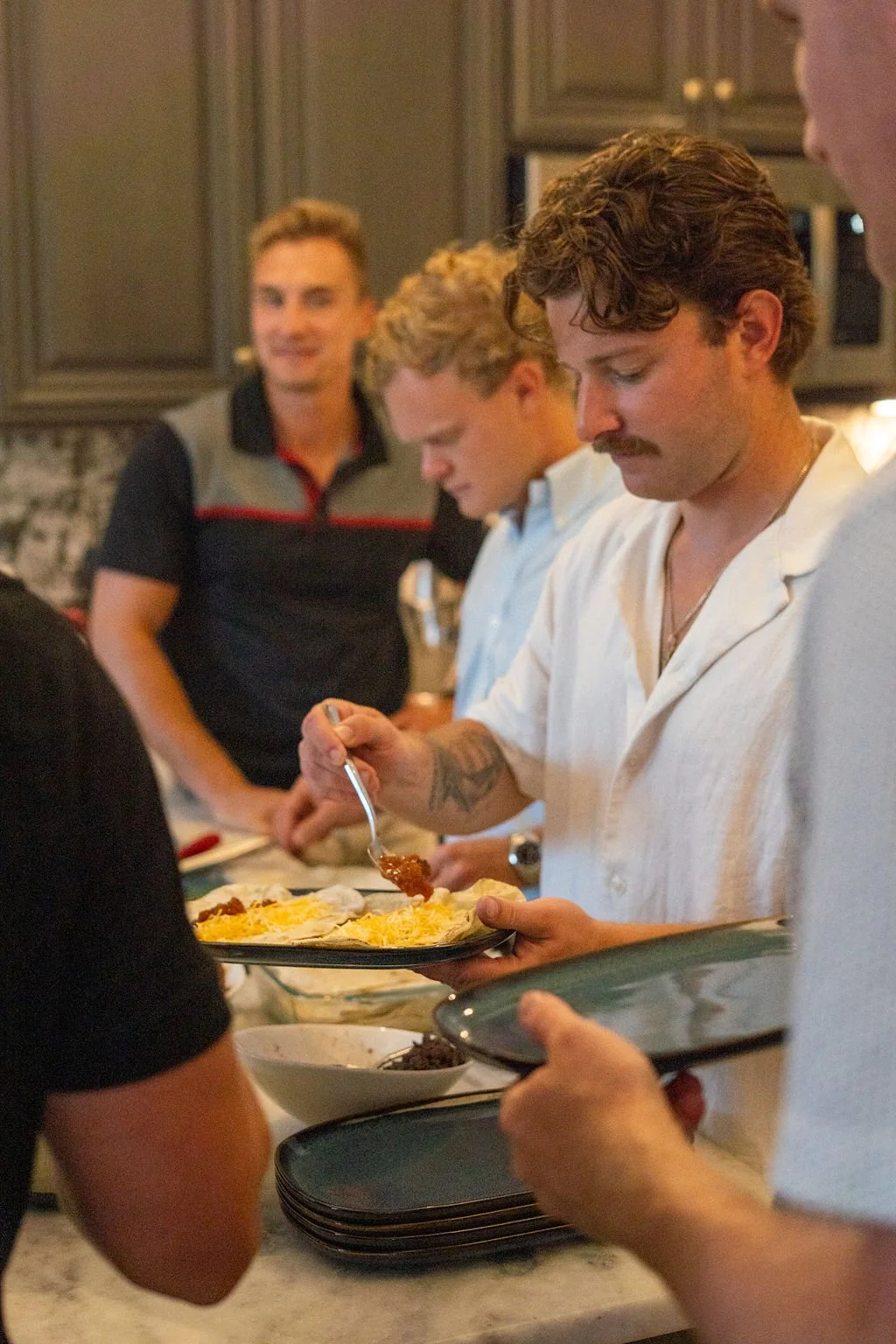 Group of men serving themselves food at a buffet table in a kitchen or dining area.