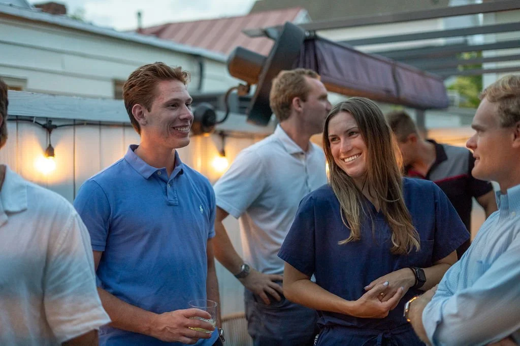 Group of young adults socializing outdoors at a gathering, smiling and engaging in conversation during evening.