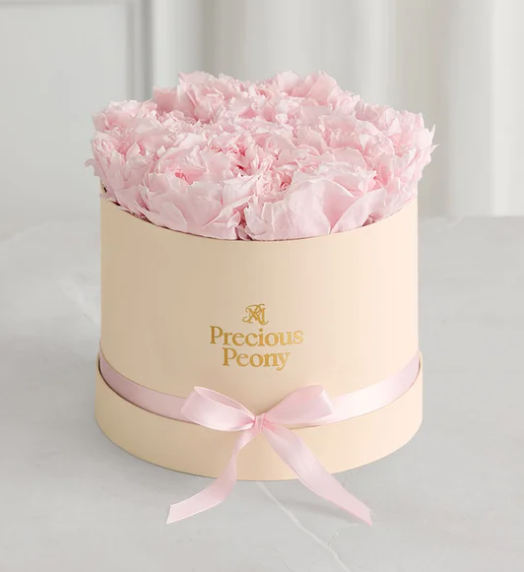 A round, cream-colored box filled with pink tissue paper designed to resemble a bouquet of peonies.