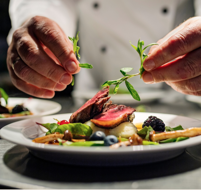 Chef garnishing plated dish with fresh herbs