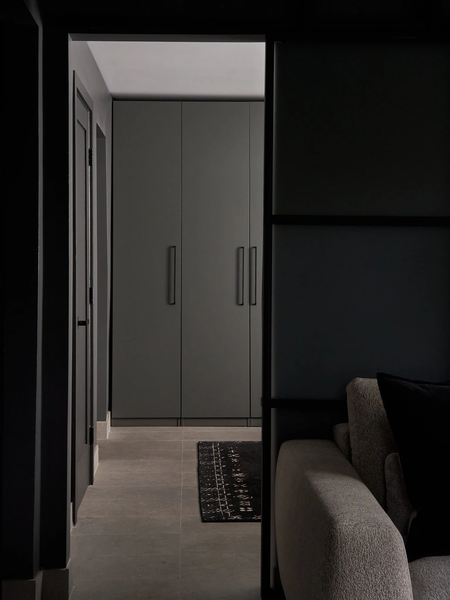 A hallway scene with a custom wardrobe, a rug, and a sofa. The scene appears in low lighting with a minimalistic and modern design.