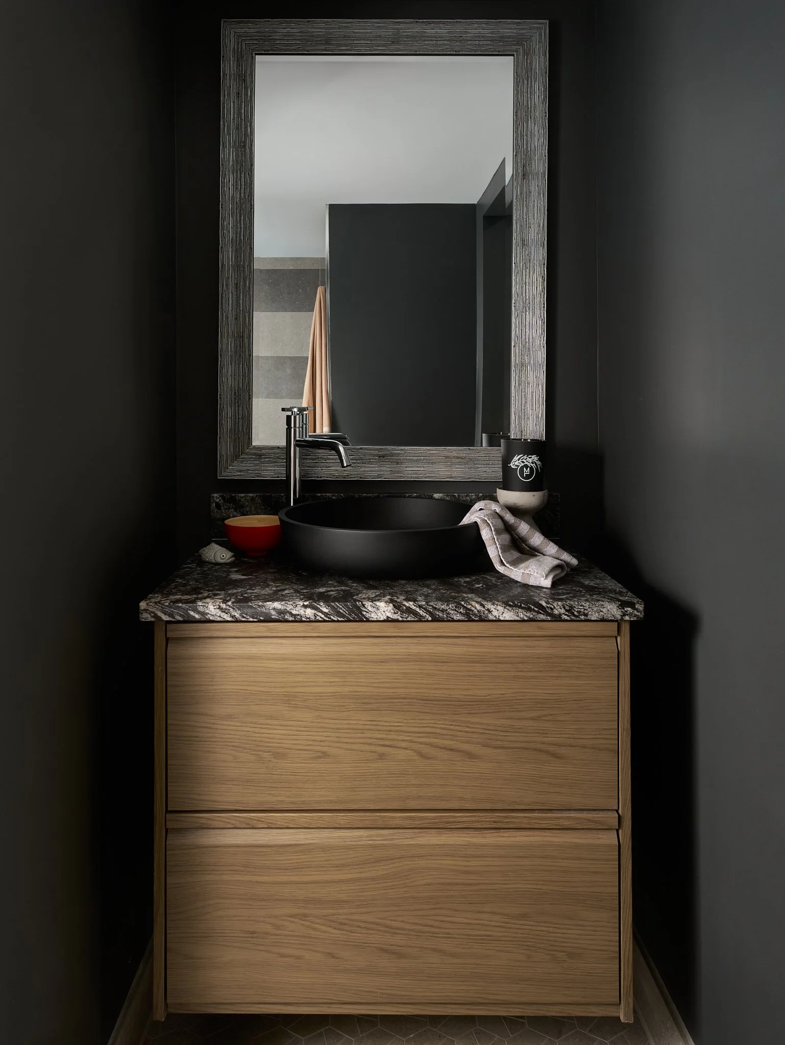 A bathroom vanity with a black vessel sink, a modern faucet, and a soap dispenser, set against dark walls with a framed mirror.