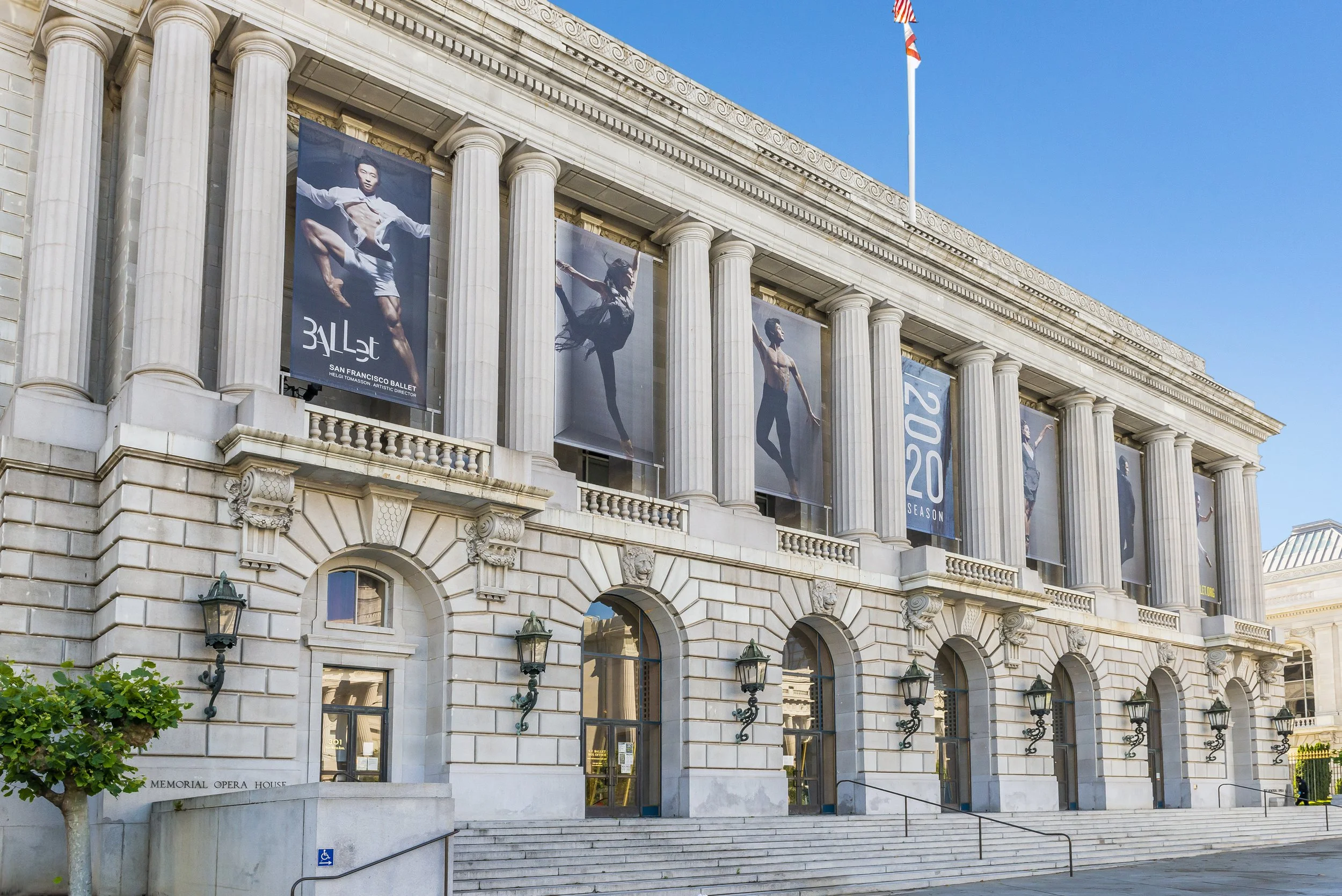 The Memorial Opera House, a historic building with grand columns, featuring banners advertising a ballet and a dance season, with clear blue sky in the background.