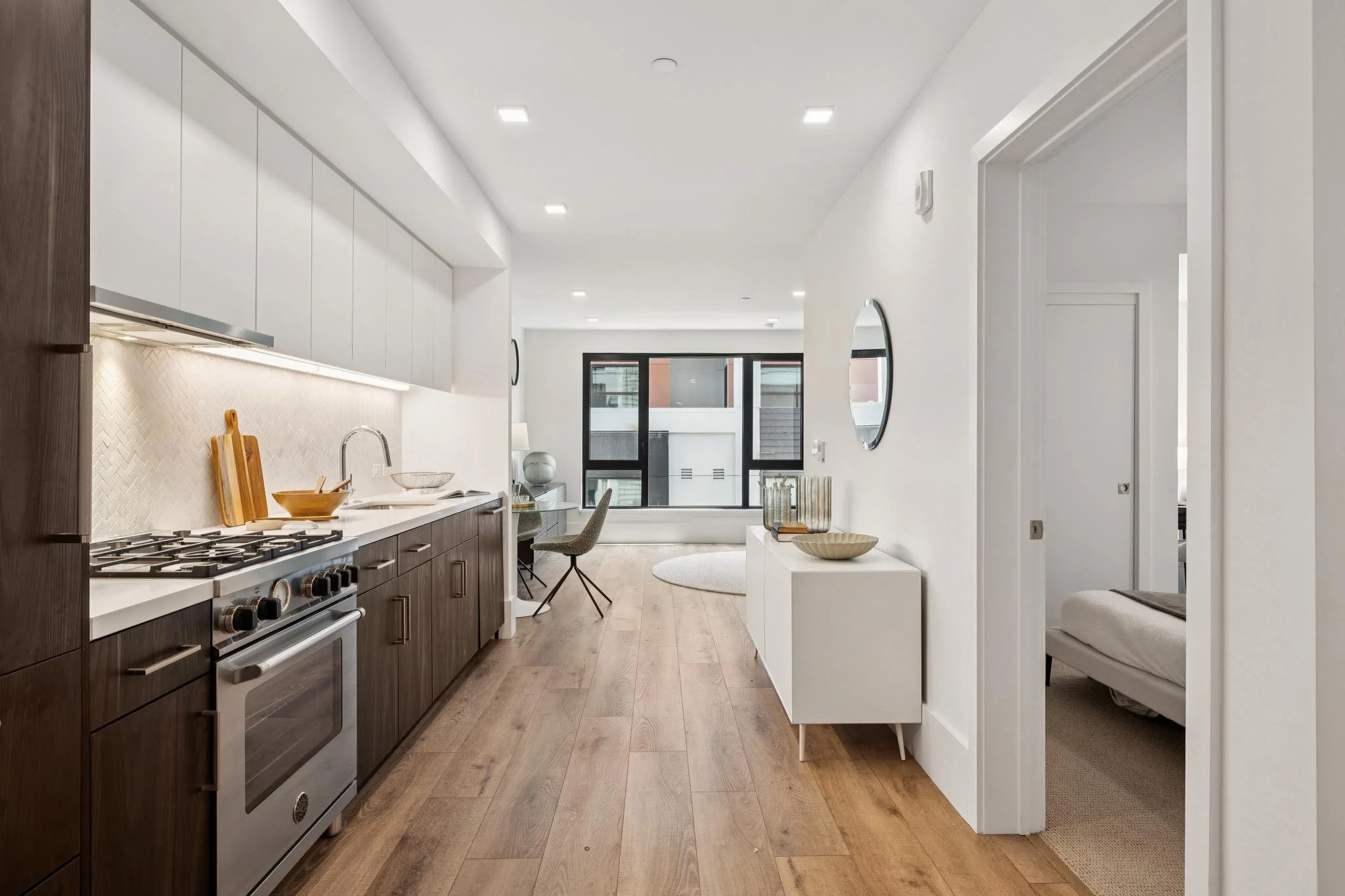 Modern kitchen and living area with white and wood cabinetry, a stove, and a window.