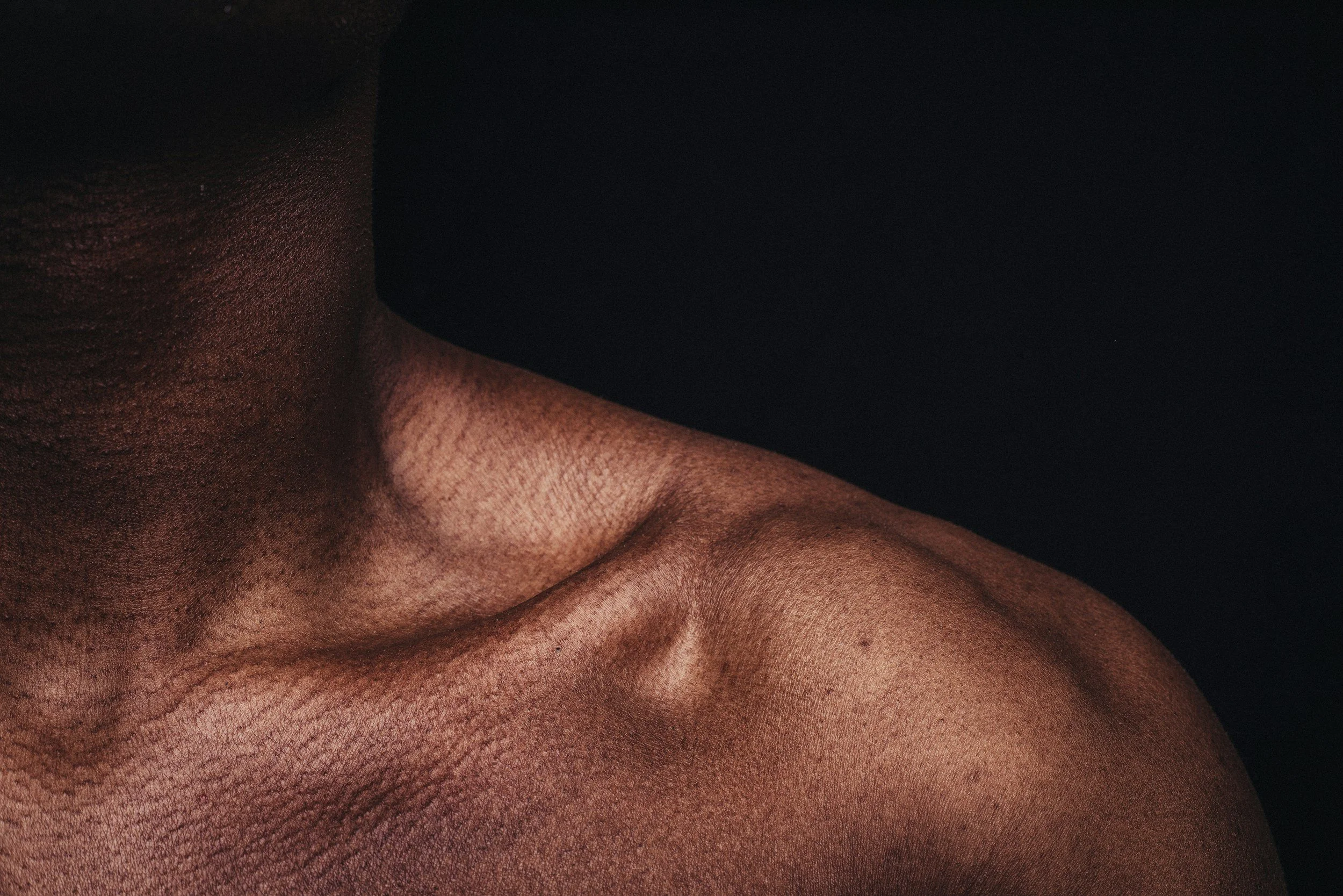 Close-up of a human arm and a hand with dark skin, showing textured skin and hair, against a black background.