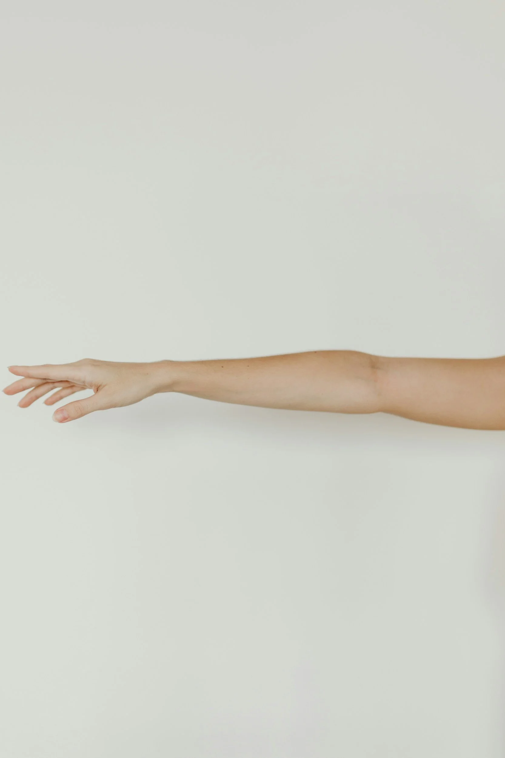 A person's outstretched arm and hand reaching to the left against a plain white background.