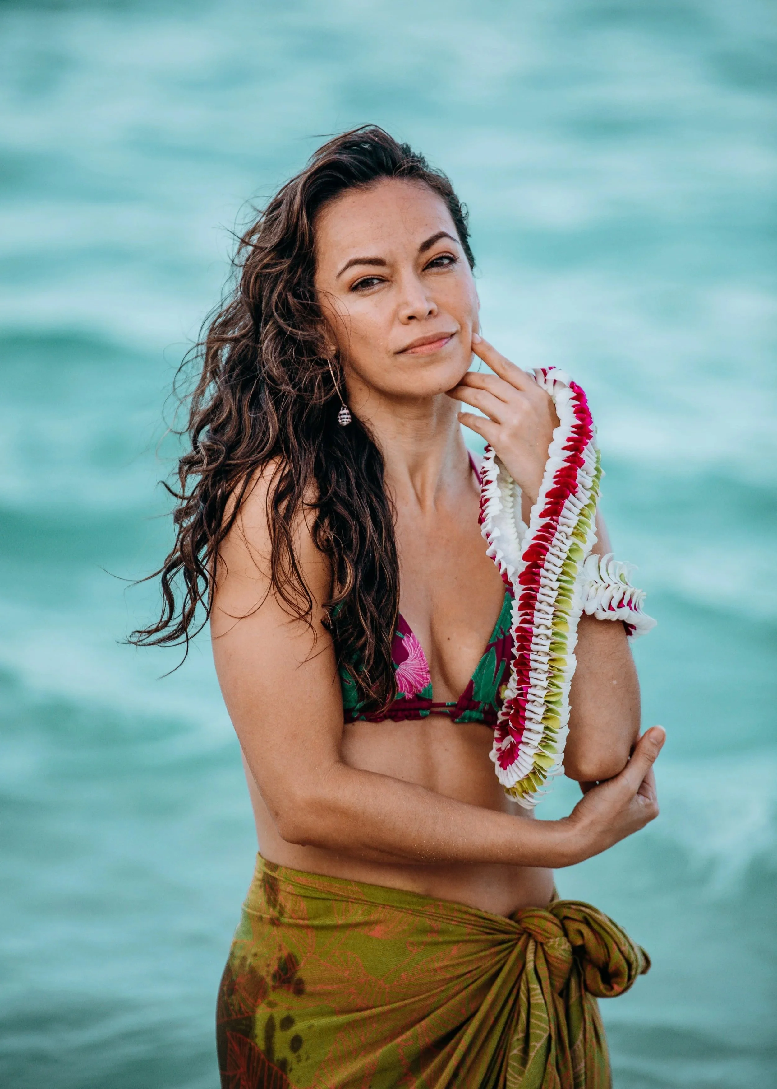 Outdoor beach portrait of a woman wearing a flower lei and tropical outfit by the ocean during a Flora & Femina session in Oʻahu.