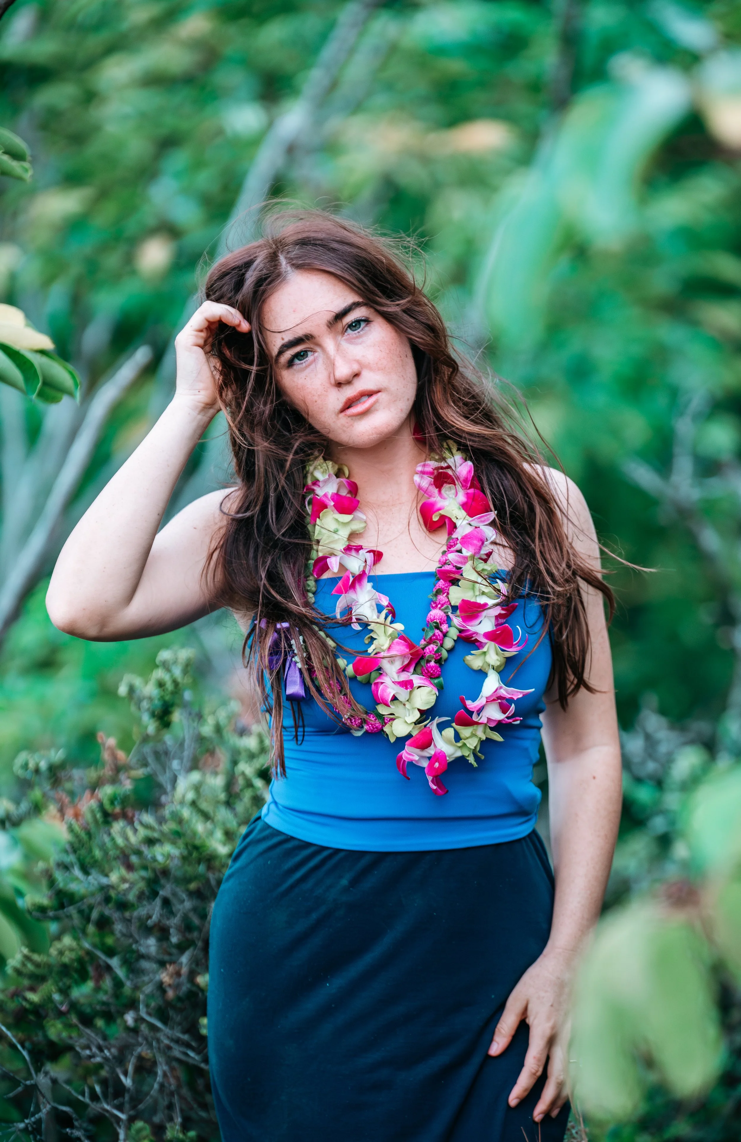 Outdoor women’s portrait with a pink and white Hawaiian flower lei surrounded by greenery during a Flora & Femina session.