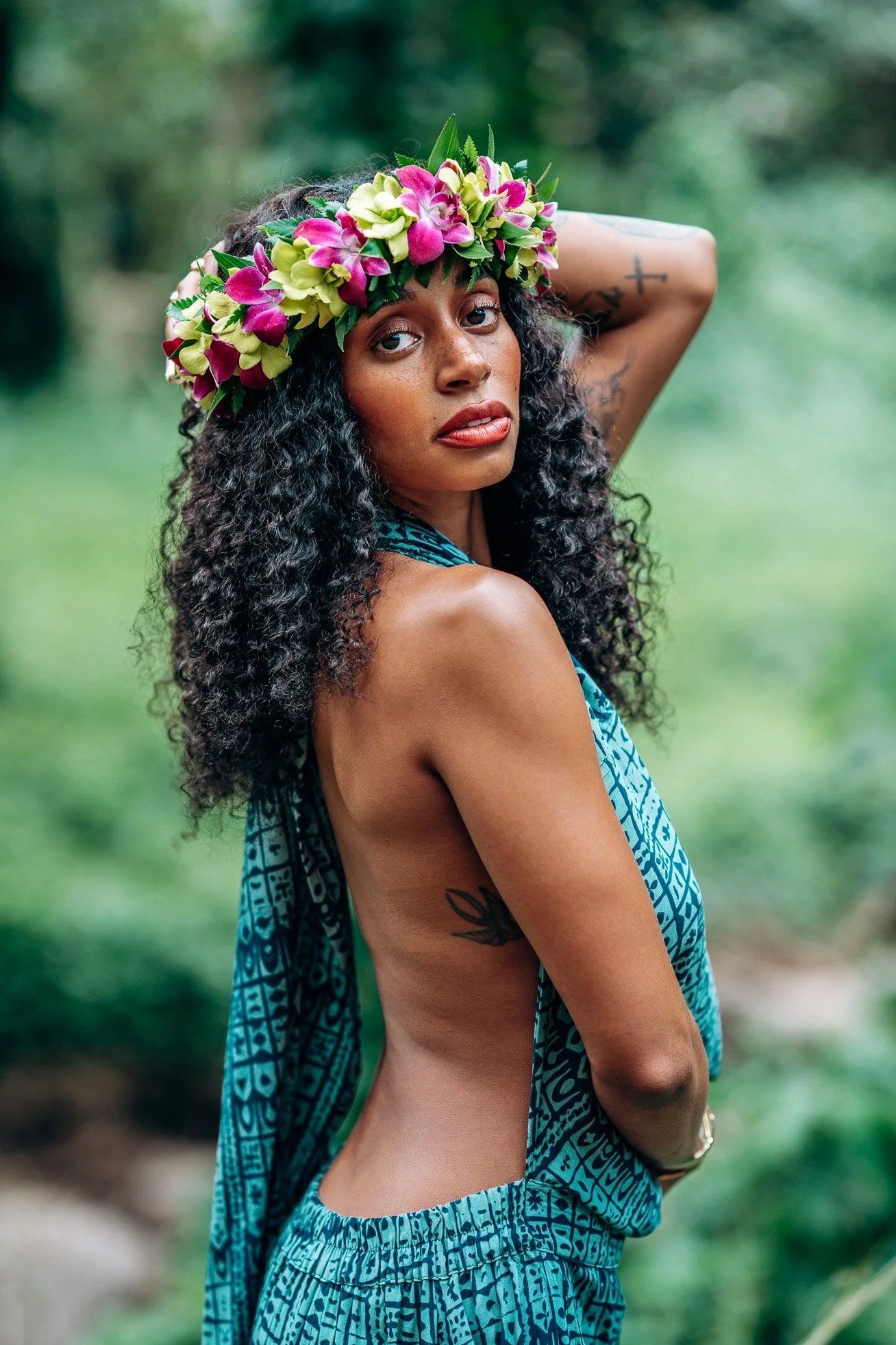Outdoor portrait of a woman wearing a colorful Hawaiian flower crown with soft greenery in the background during a Flora & Femina portrait session.