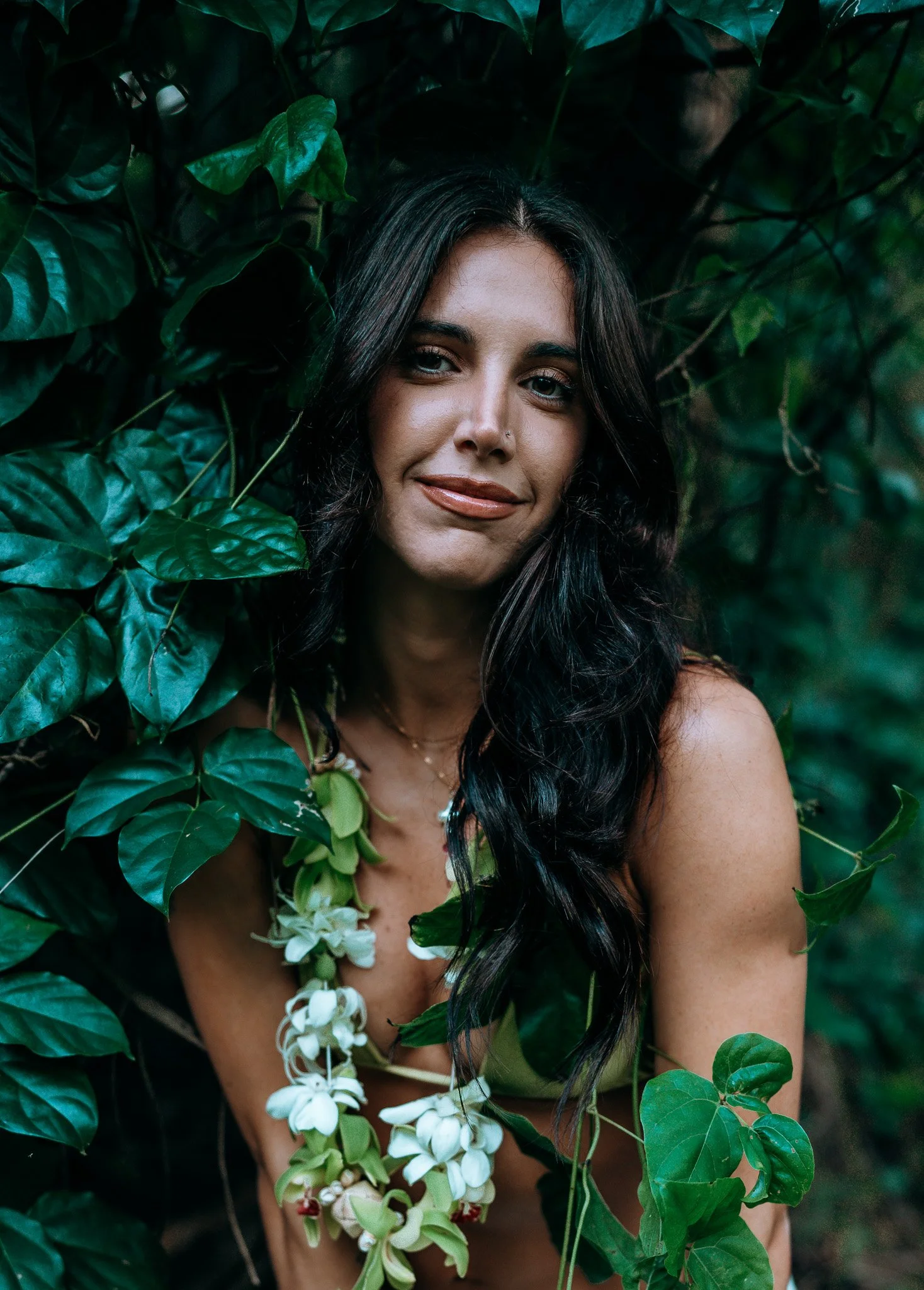 Tropical portrait of a woman framed by green leaves and white flowers in a lush jungle setting during a Flora & Femina session.