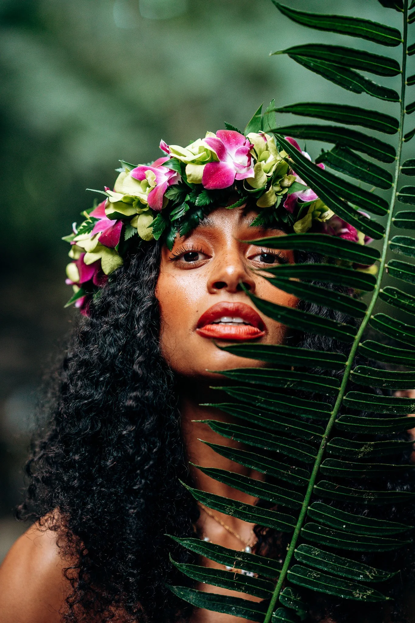 Floral portrait of a woman wearing a pink and green flower crown surrounded by tropical leaves during a Flora & Femina session.