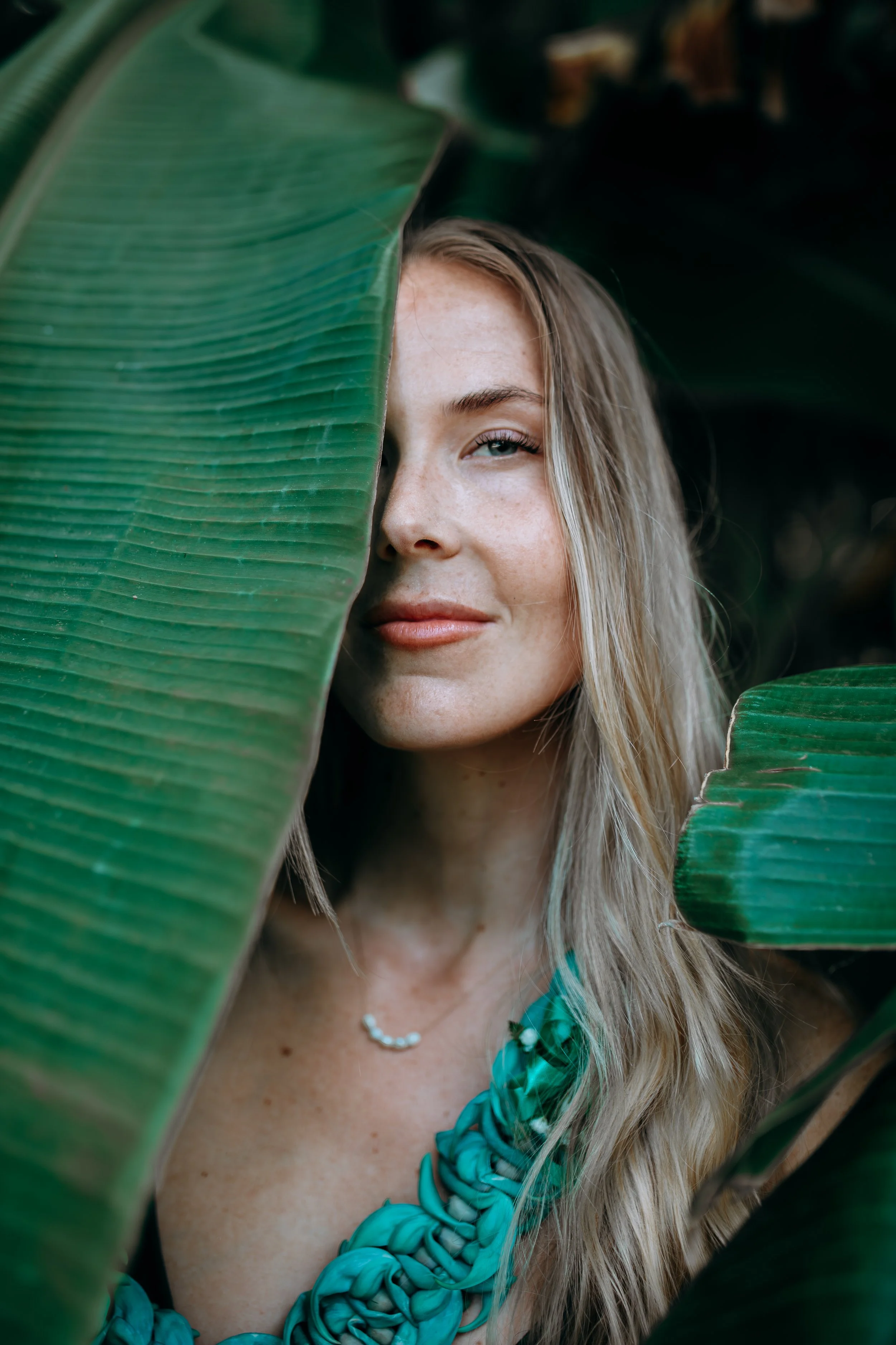 Outdoor portrait of a woman framed by large tropical green leaves during a Flora & Femina session in a lush natural setting.