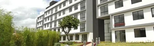 Edificio moderno de varios pisos con jardín y árboles en un entorno urbano.