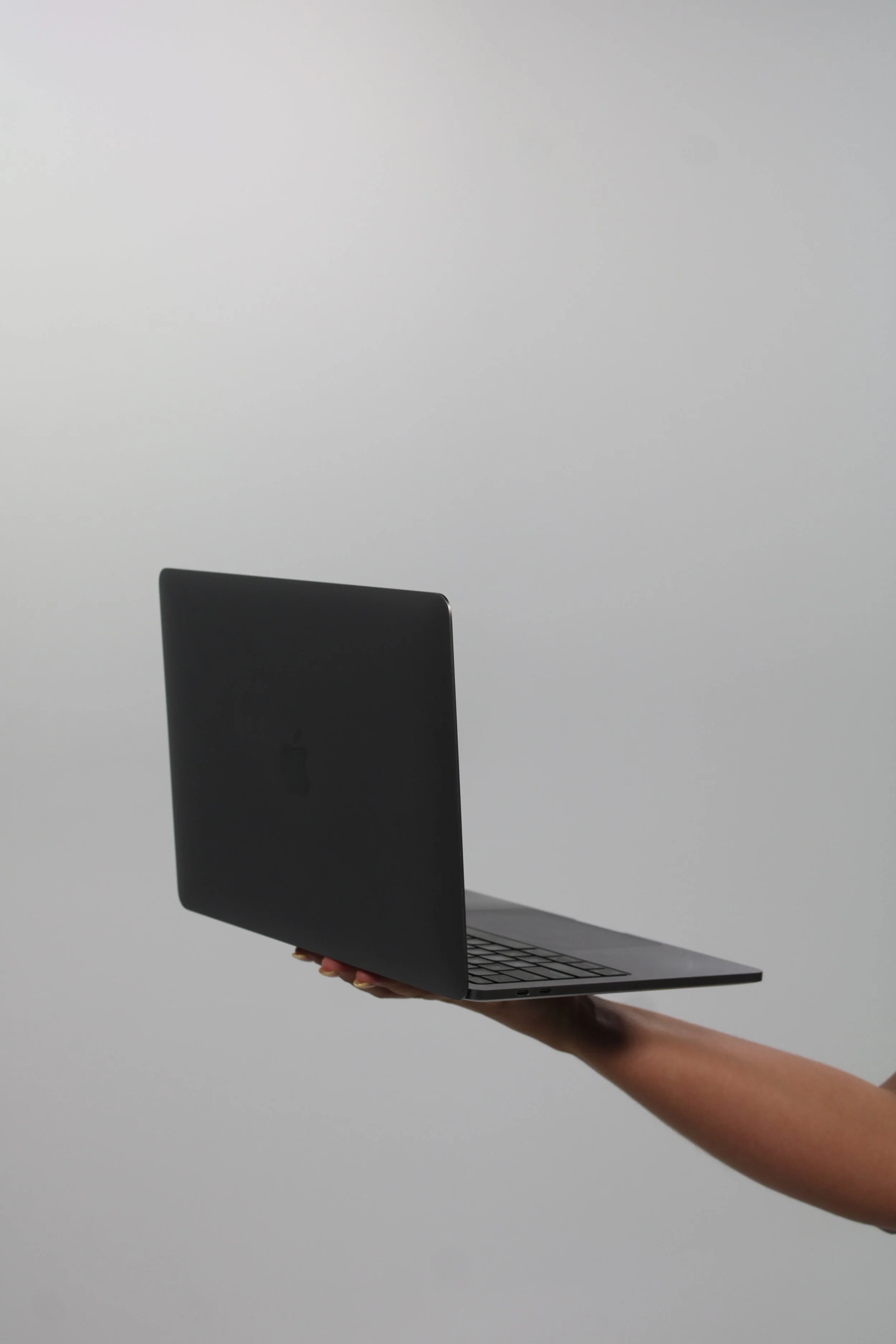 A person holding an open laptop in front of a plain white background.