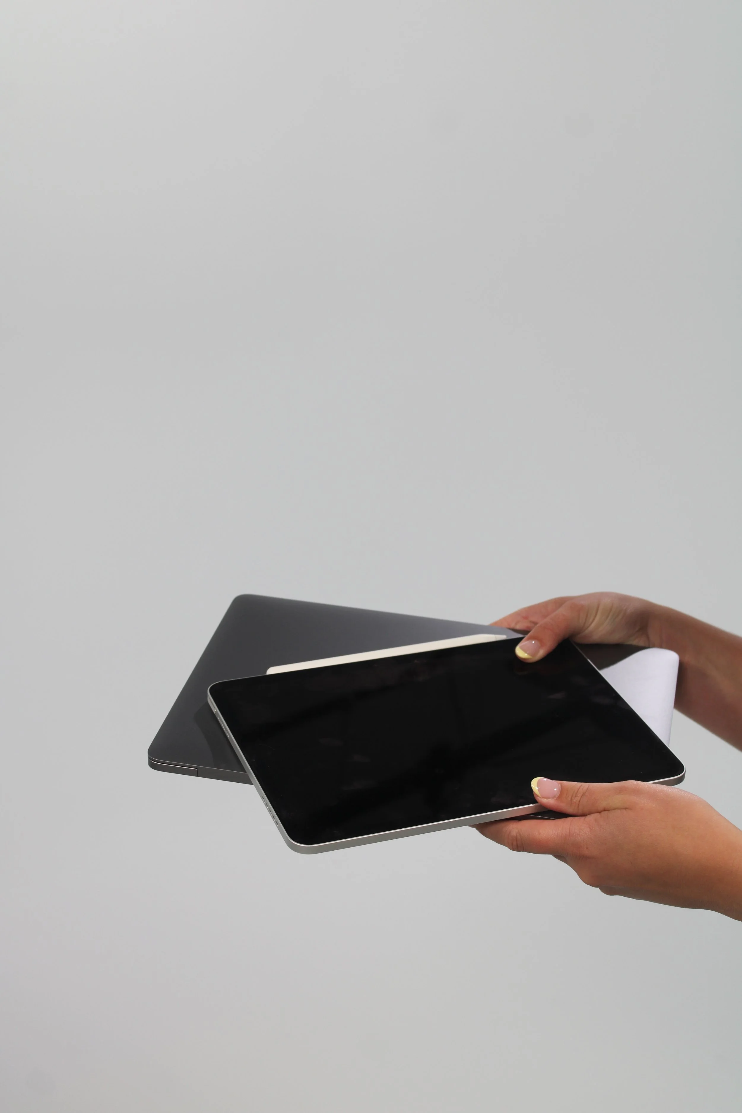Two hands holding different electronic tablets with a gray wall in the background.