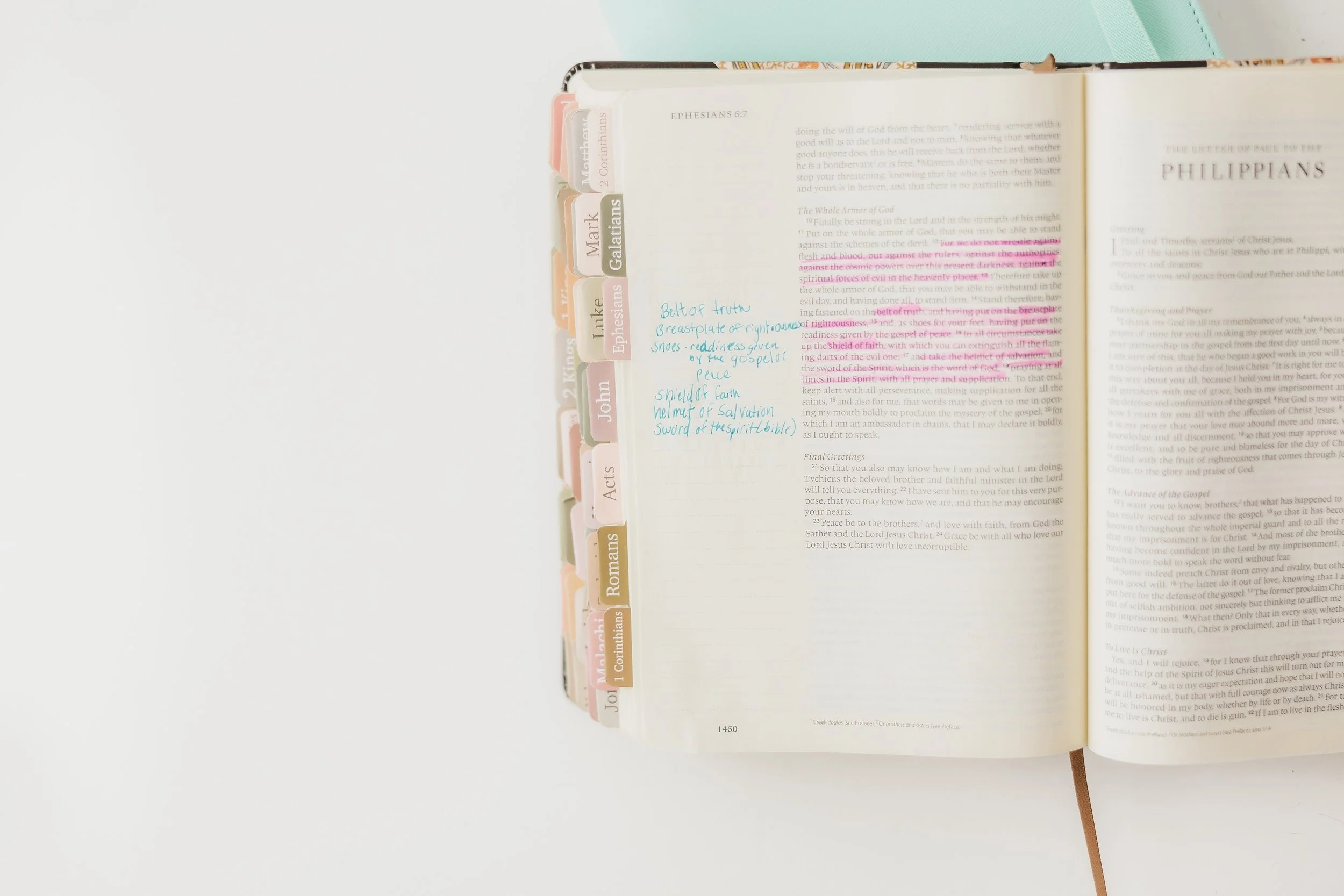 Open Bible with colorful tab labels on the left side, handwritten notes in blue ink on the page, resting on a white surface.