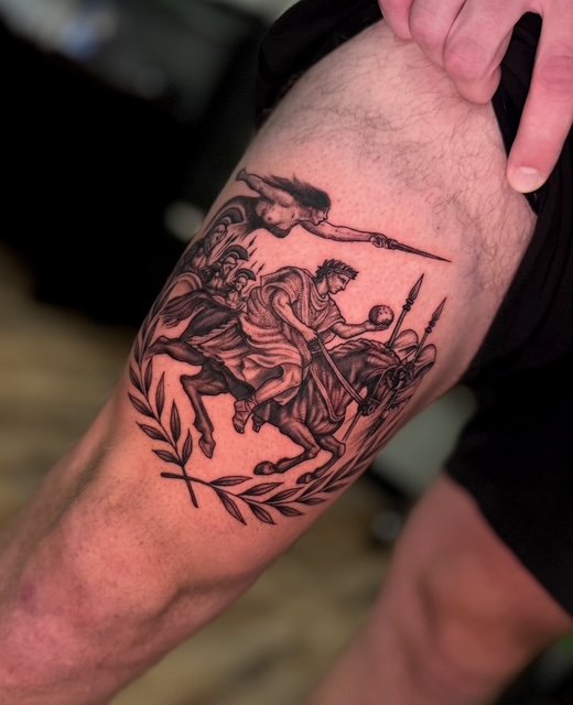 Tattoo of a person riding a horse with a spear, accompanied by a winged figure and a celestial body, with decorative leaves surrounding the scene.