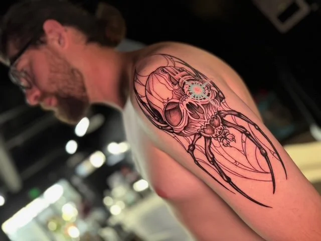 Tattoo of a detailed, stylized skull with mechanical and insect-like elements on a man's upper arm and shoulder.