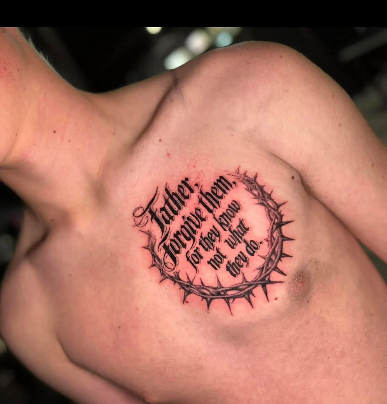 Close-up of a person's upper chest with a tattoo that reads, 'Heart does for those them, not they know not when they will do,' surrounded by a thorny circular design.