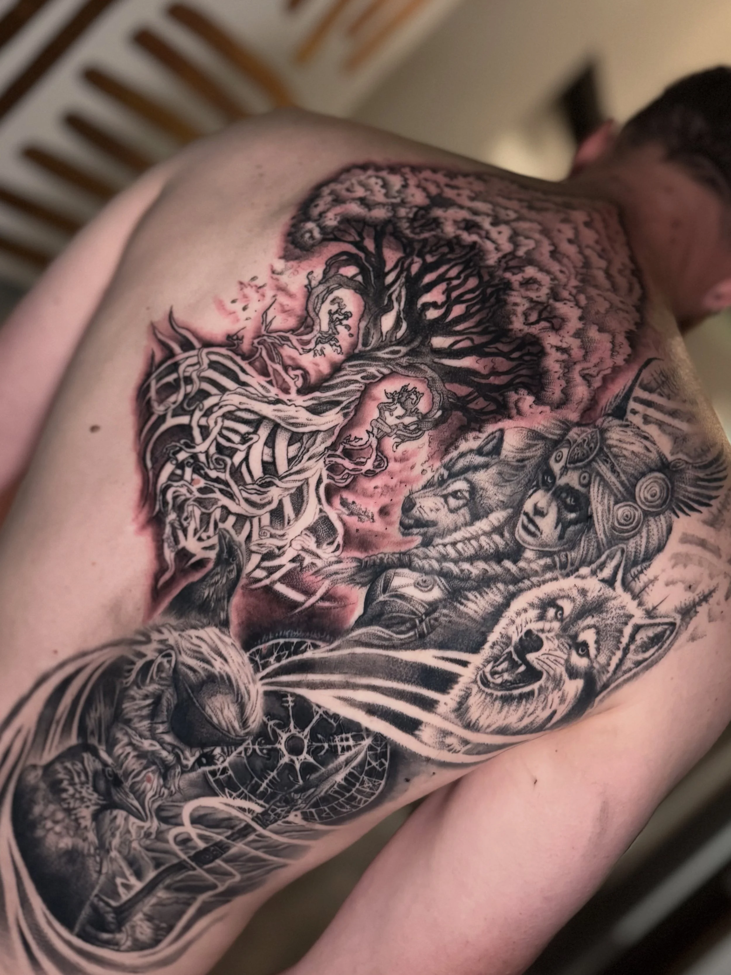 A detailed black and gray tattoo of a tree with sprawling roots and branches on a person's arm.