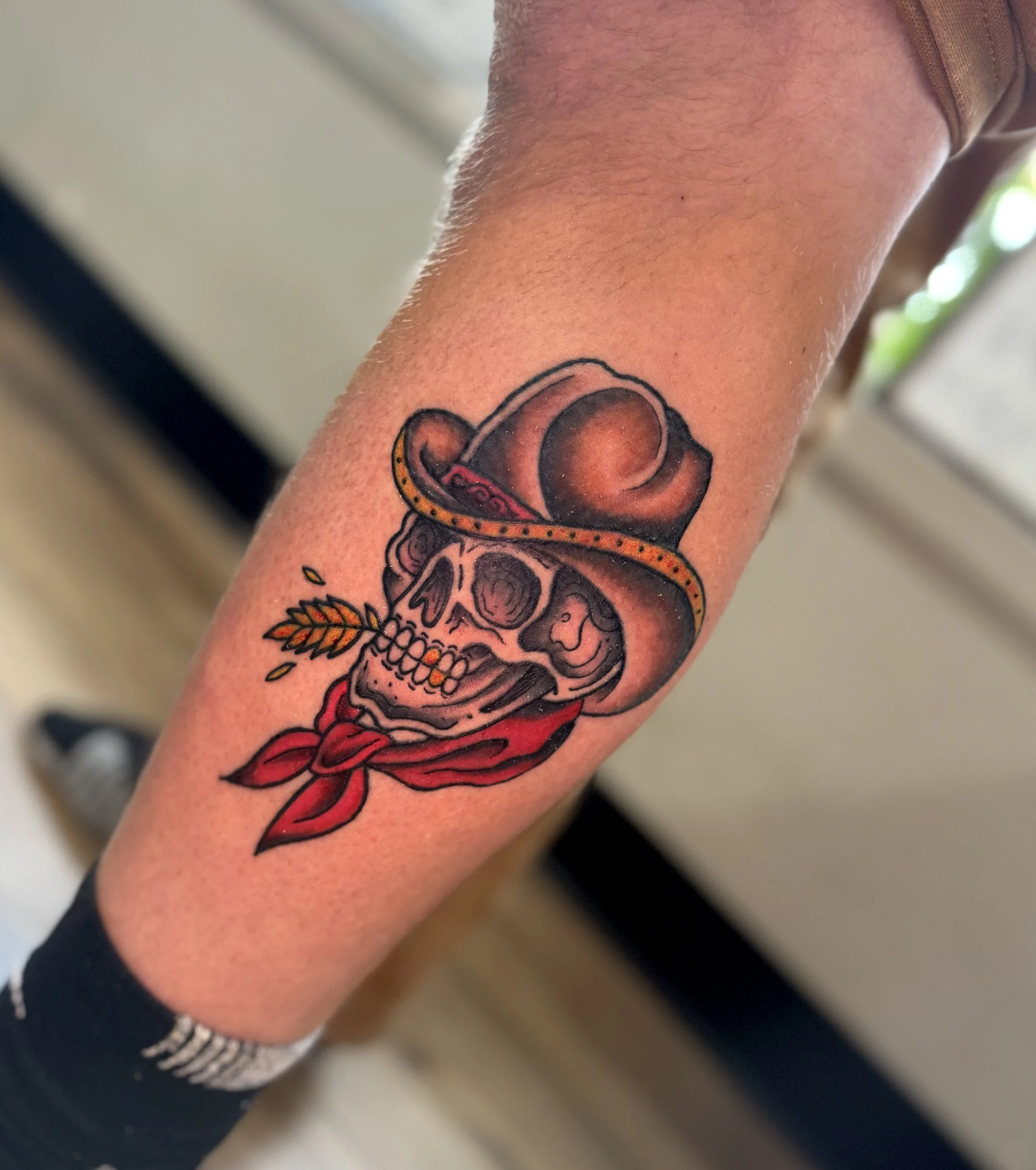 Tattoo of a skull with a red bandana and a sheriff's badge on a person's arm.