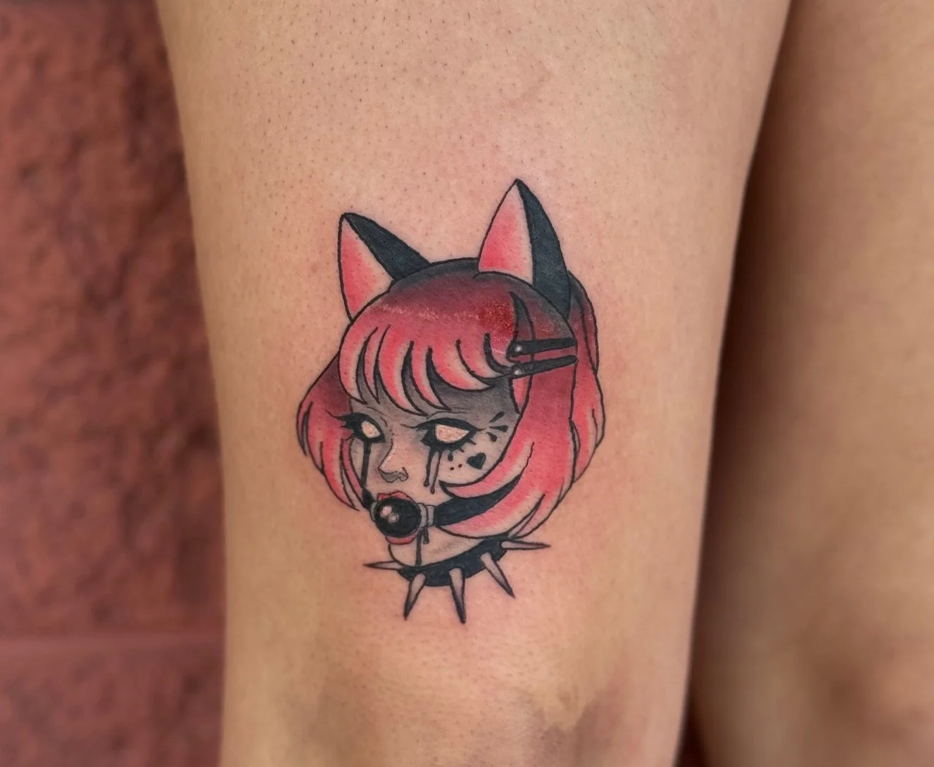 Tattoo of a girl with cat ears, wearing a collar with spikes, with tears on her face, colored in black and pink on skin.