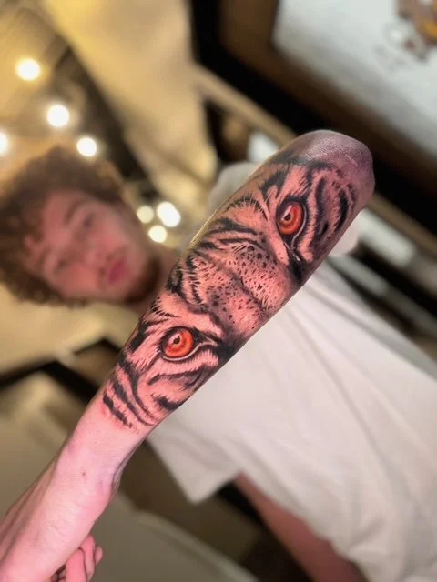 Tattoo of tiger eyes on a person's finger with a blurred person and Christmas lights in the background.