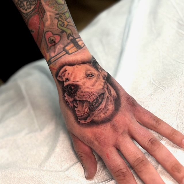 Tattoo of a happy, smiling dog on a person's hand.