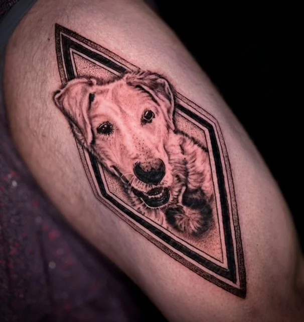 Tattoo of a puppy inside a geometric frame on a person's skin.